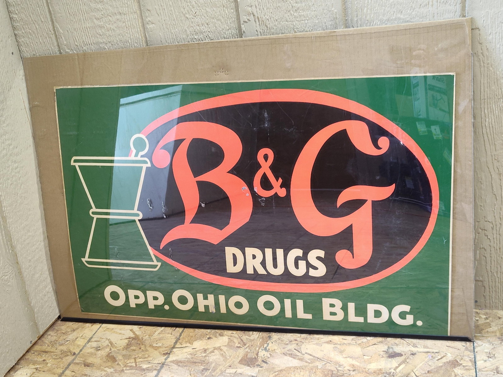 B&G Drugs Pharmaceutical Sign w/ Ohio Oil Building: This is a mid-20th-century pharmaceutical advertising sign for B&G Drugs. The sign features a dark green background with a central black oval containing a stylized B and G logo in coral-orange font.