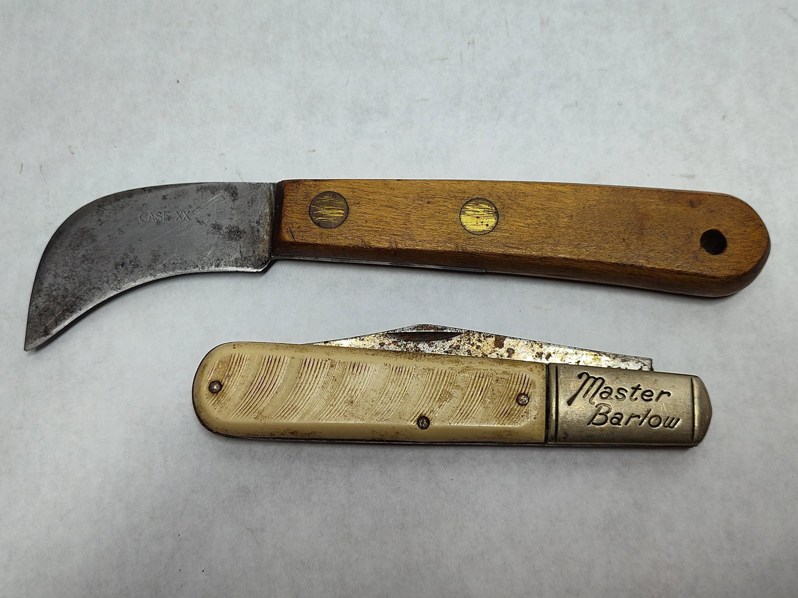 Pair Case XX Hawkbill & Colonial Barlow Knives: This lot features two utility knives of American manufacture. The first is a fixed blade hawkbill pruning or linoleum knife by W.R. Case and Sons Cutlery Co., marked with the CASE XX blade stamp. It