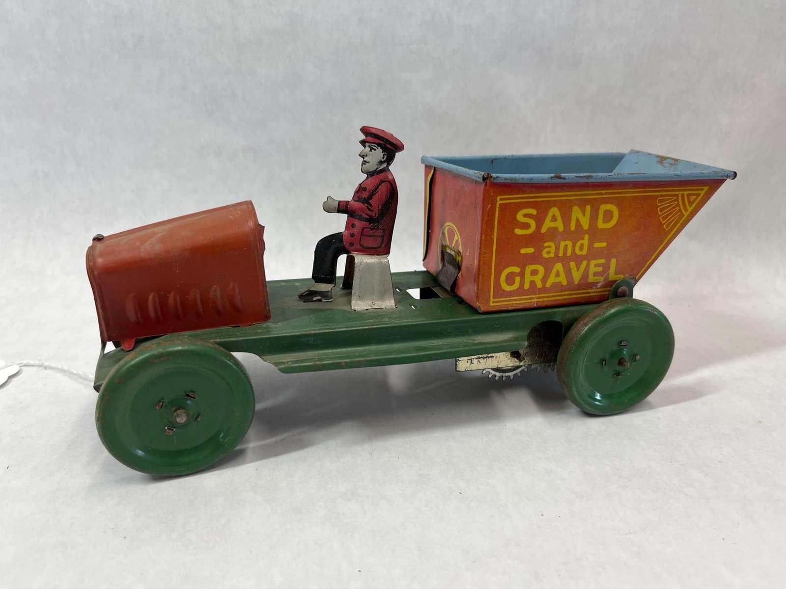 Marx Toys Wind-Up Tin Lithograph Sand and Gravel Dump Truck: Manufactured by Louis Marx and Co., this wind-up toy is a lithographed tin dump truck. The vehicle features a green chassis with matching green wheels and a red hood. The red dump bed has a light