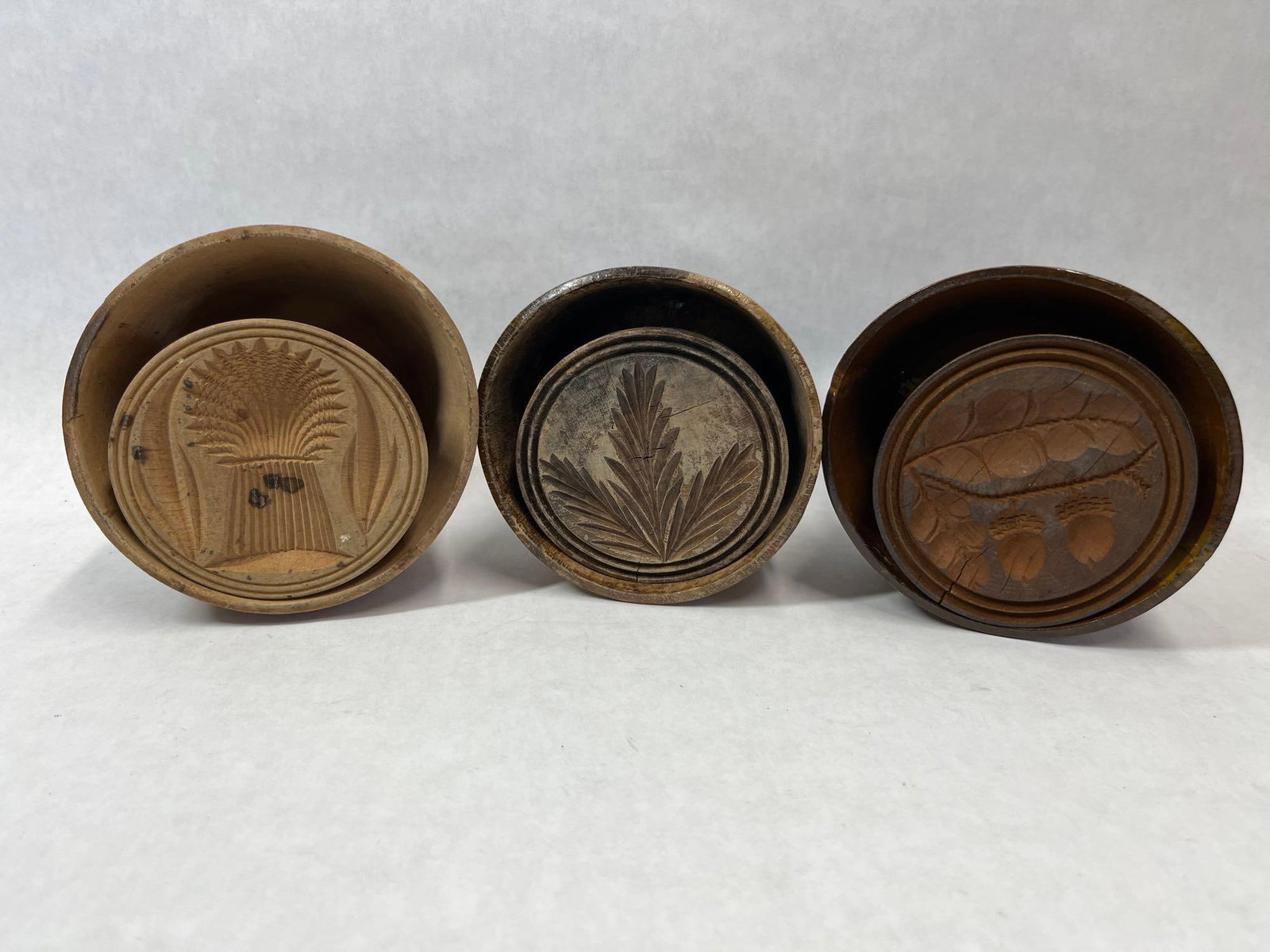 Trio Antique Carved Wood Plunger Butter Molds: This lot comprises a trio of antique wooden butter stamps, each complete with its original cylindrical sleeve and plunger mechanism. Carved from solid hardwood, these kitchen implements exhibit a
