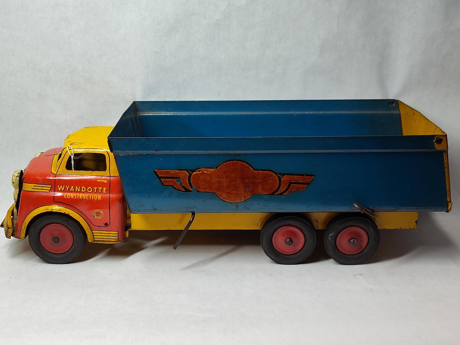 Wyandotte Chieftain Lines Tandem Axle Dump Truck: This toy is a Wyandotte Toys (All Metal Products Co.) Chieftain Lines construction dump truck. The vehicle is constructed of pressed steel and features a red cab with a yellow roof and chassis, suppor