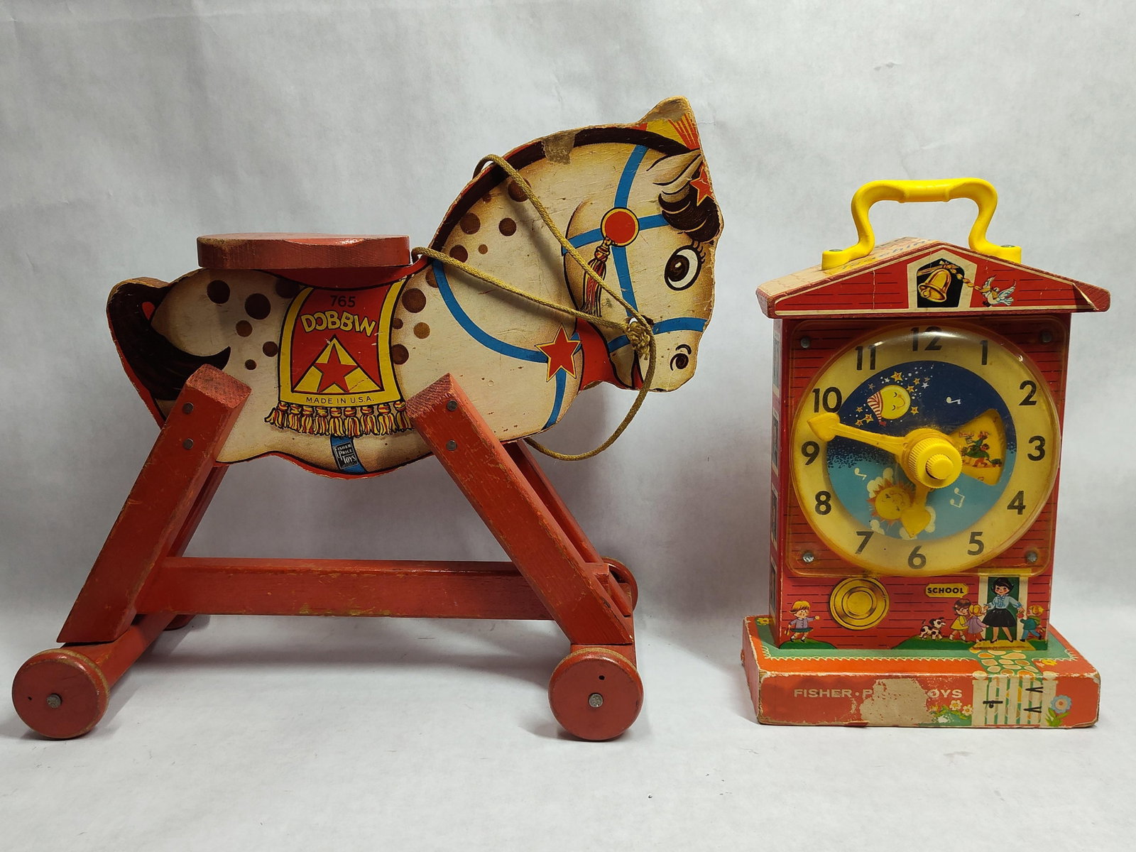 Pair Fisher-Price: Dobbin & Music Box Clock: This lot consists of two toys manufactured by Fisher-Price. The first item is a Dobbin Horse pull toy, model number 765, featuring a wooden body with lithographed paper overlays. The horse is mounted 