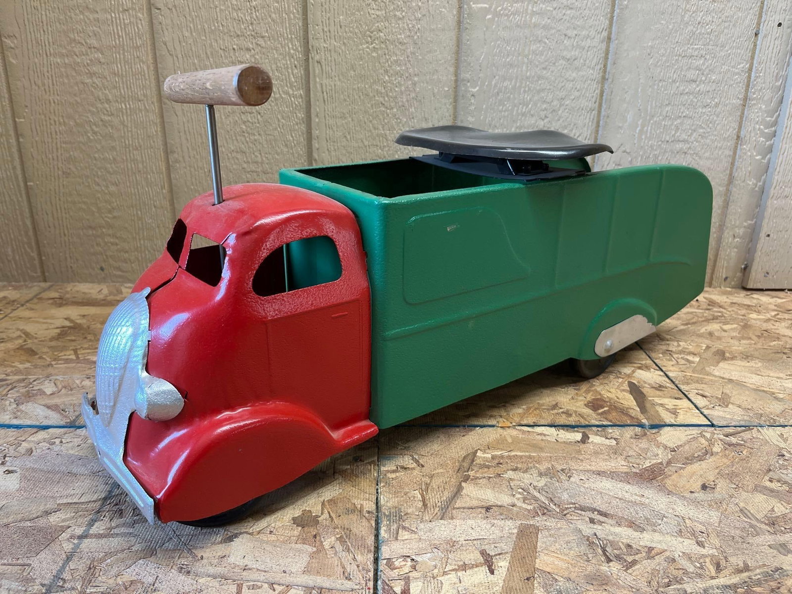 Art Deco Style Pressed Steel Ride-On Toy Truck: This large-scale ride-on toy truck features a streamlined Art Deco design, specifically a Cab Over Engine style modeled after 1930s Studebaker trucks. The item is constructed from pressed steel and