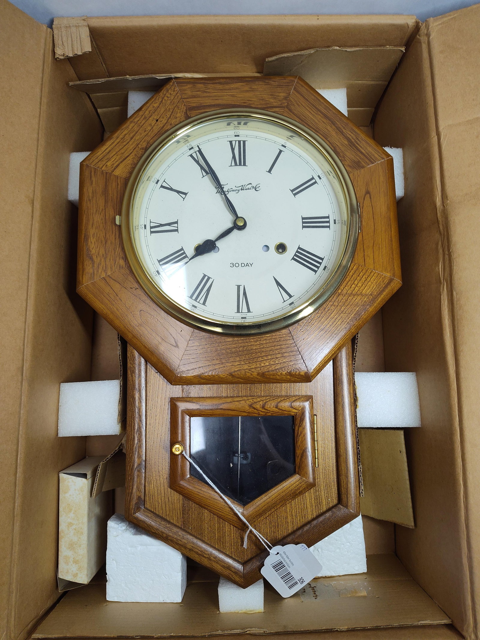 Montgomery Ward & Co. Schoolhouse Regulator Clock: This schoolhouse style drop-trunk regulator wall clock is produced by Montgomery Ward and Co. The case is constructed of wood with a warm oak-colored finish, featuring an octagonal top and a lower