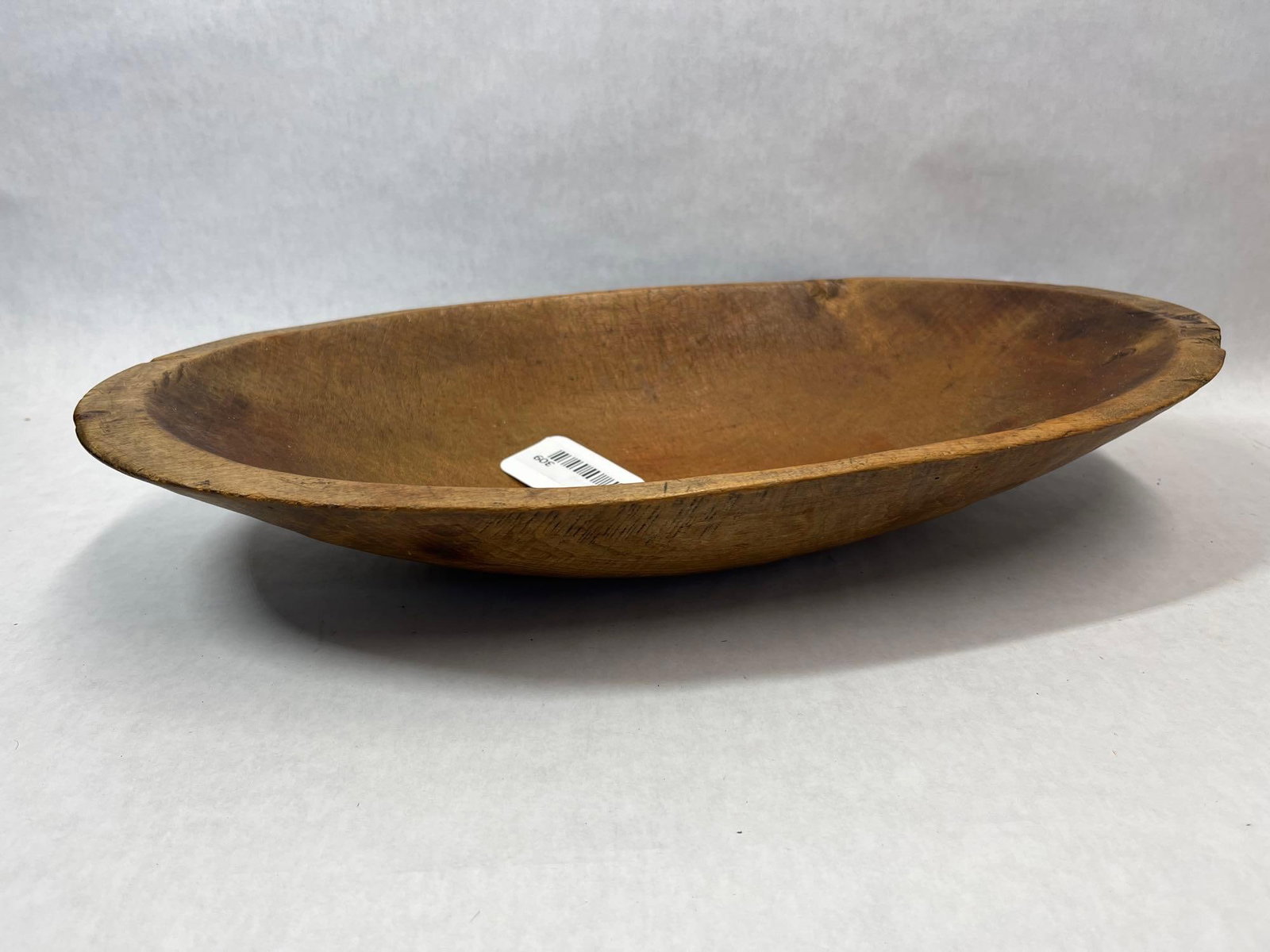 American Primitive Carved Wood Oval Dough Bowl: An antique American primitive-style wooden dough bowl or trencher of elongated oval form, hand-carved from a single piece of wood. The object features a shallow, scooped interior with visible tool mar