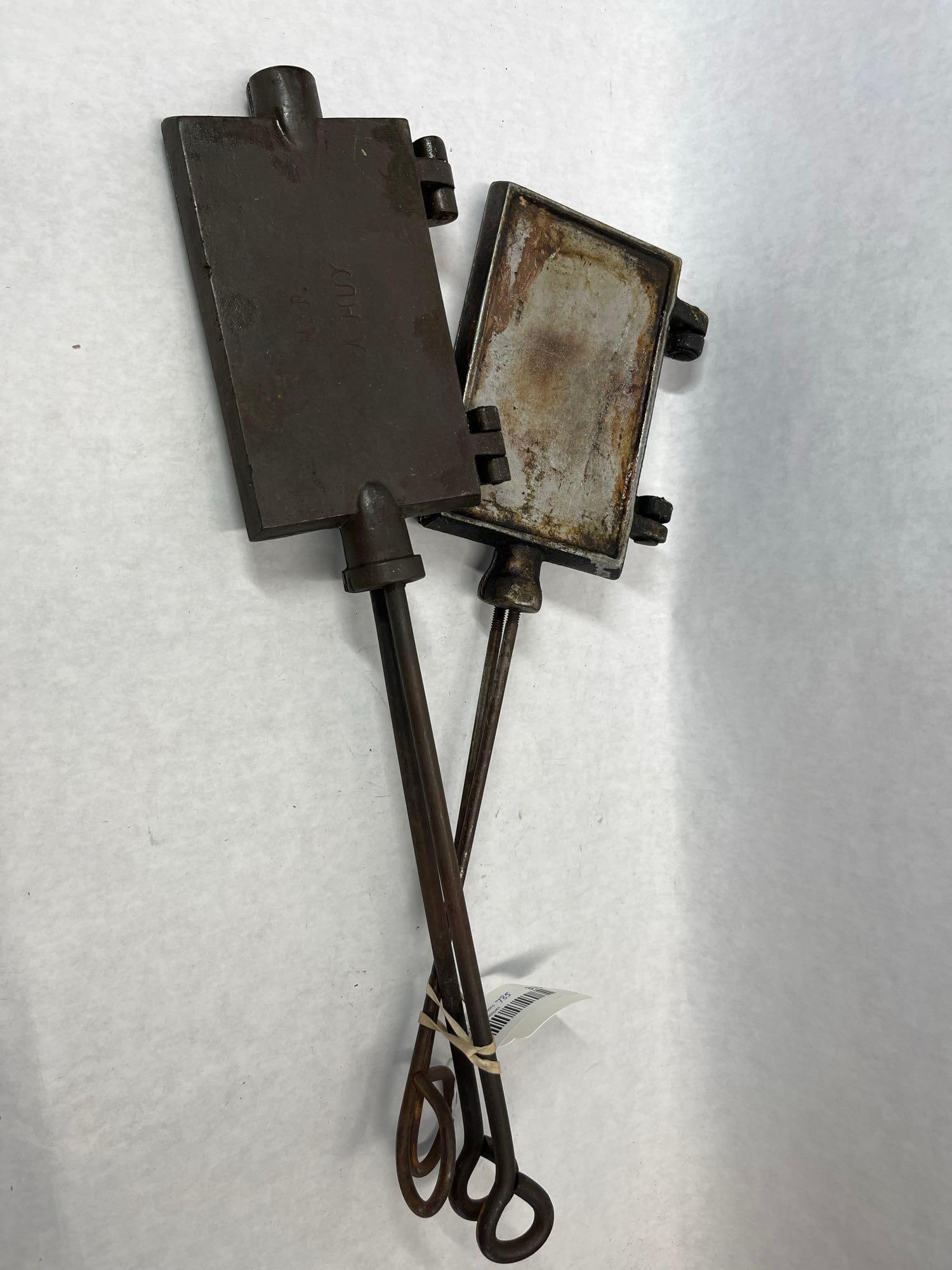 Pair Huy Belgian Cast Iron Waffle & Galette Irons: Two antique Belgian cast iron cooking irons designed for hearth or campfire use. One iron features a rectangular hinged head with a symmetrical waffle-grid pattern on both interior faces; its exterior