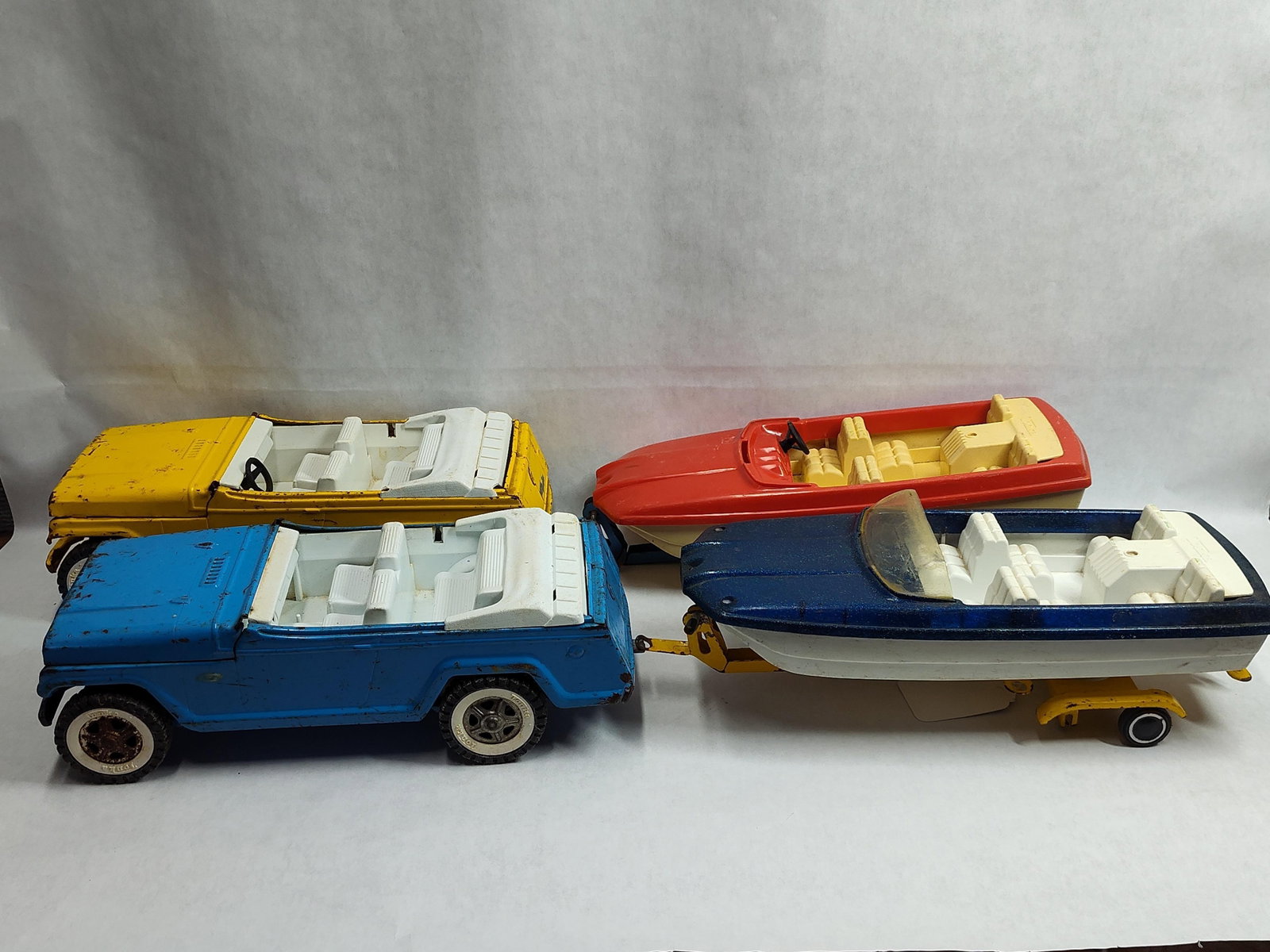 Tonka Jeepster & Runabout Boat Trailer Sets: A collection of Tonka toys featuring two Jeepster-style vehicles and two Runabout speedboat sets. The items are constructed from a combination of pressed steel and molded plastic. The collection