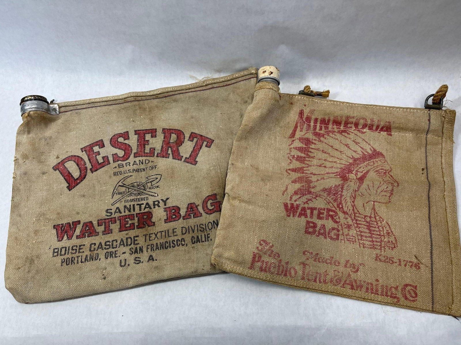 Pair Boise Cascade & Pueblo Tent Canvas Water Bags: This lot features two canvas evaporative water bags, which were essential accessories for mid-century desert travel and camping. The first bag is a Desert Brand Sanitary Water Bag, produced by the