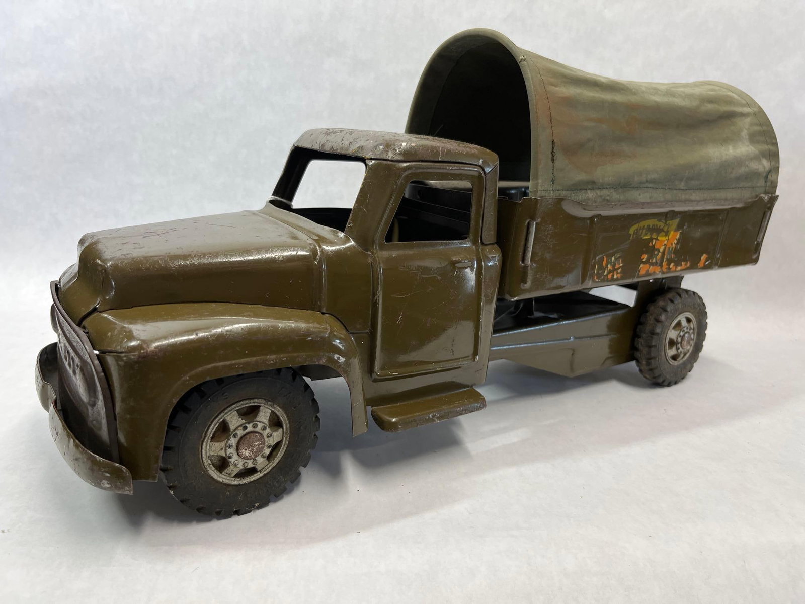 Buddy L Army Transport Truck with Canvas Canopy: This toy is a Buddy L Army Transport Truck constructed from pressed steel. The vehicle features a single cab design with an open interior and a rear cargo bed. A green canvas canopy covers the bed,