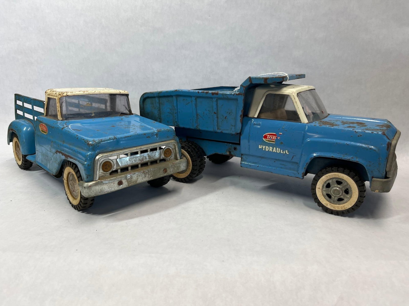 Pair Tonka Steel Hydraulic Dump & Stake Trucks: This lot features two trucks manufactured by Tonka Toys in Mound, Minnesota, likely dating to the 1960s. The first item is a Tonka Hydraulic Dump Truck, identified by the incised Tonka name on the fro