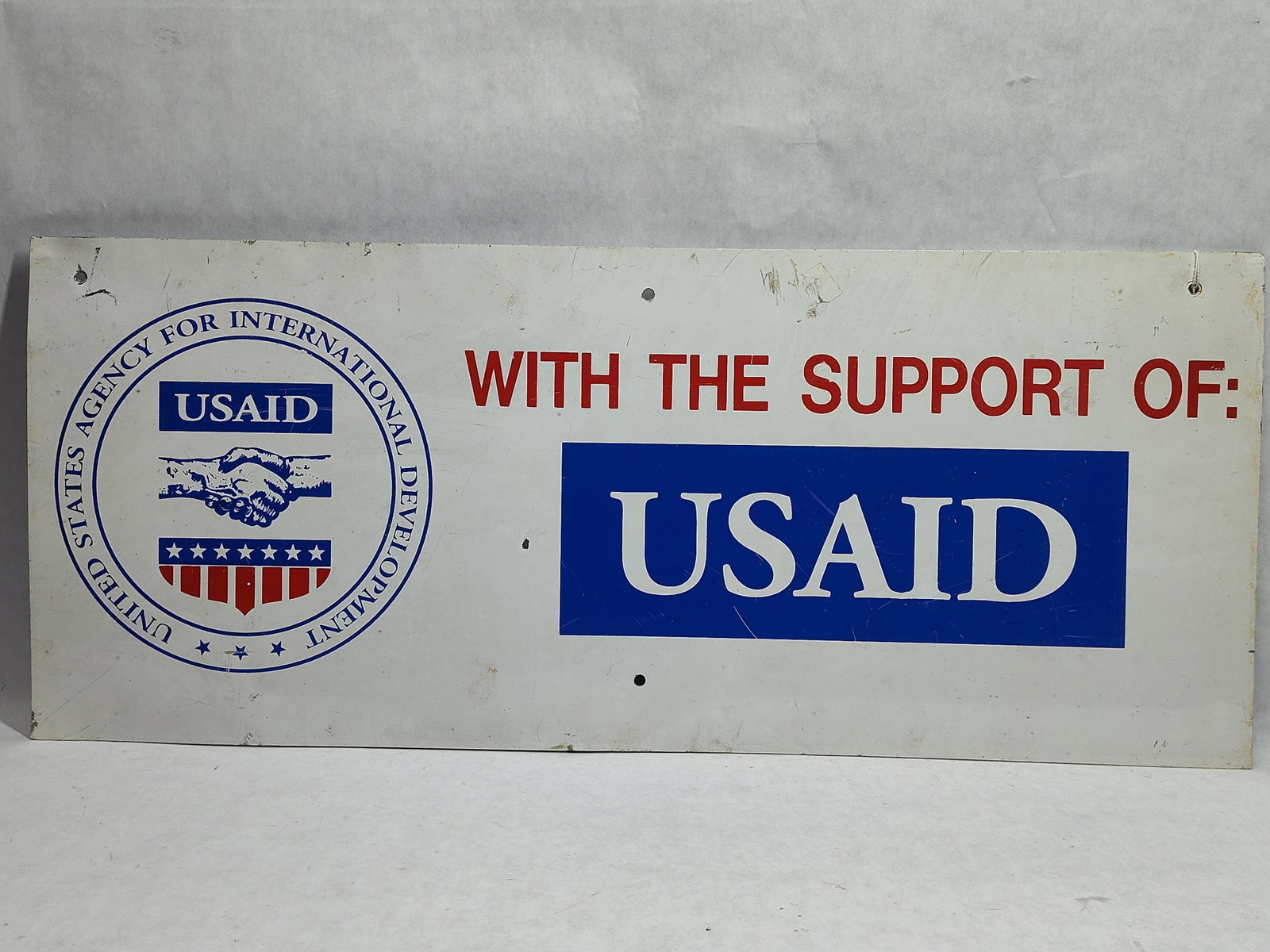 USAID U.S. Agency Int. Dev. Painted Metal Sign: A painted metal sign from the United States Agency for International Development (USAID). This rectangular, horizontal sign is constructed from sheet metal and features the official agency seal on
