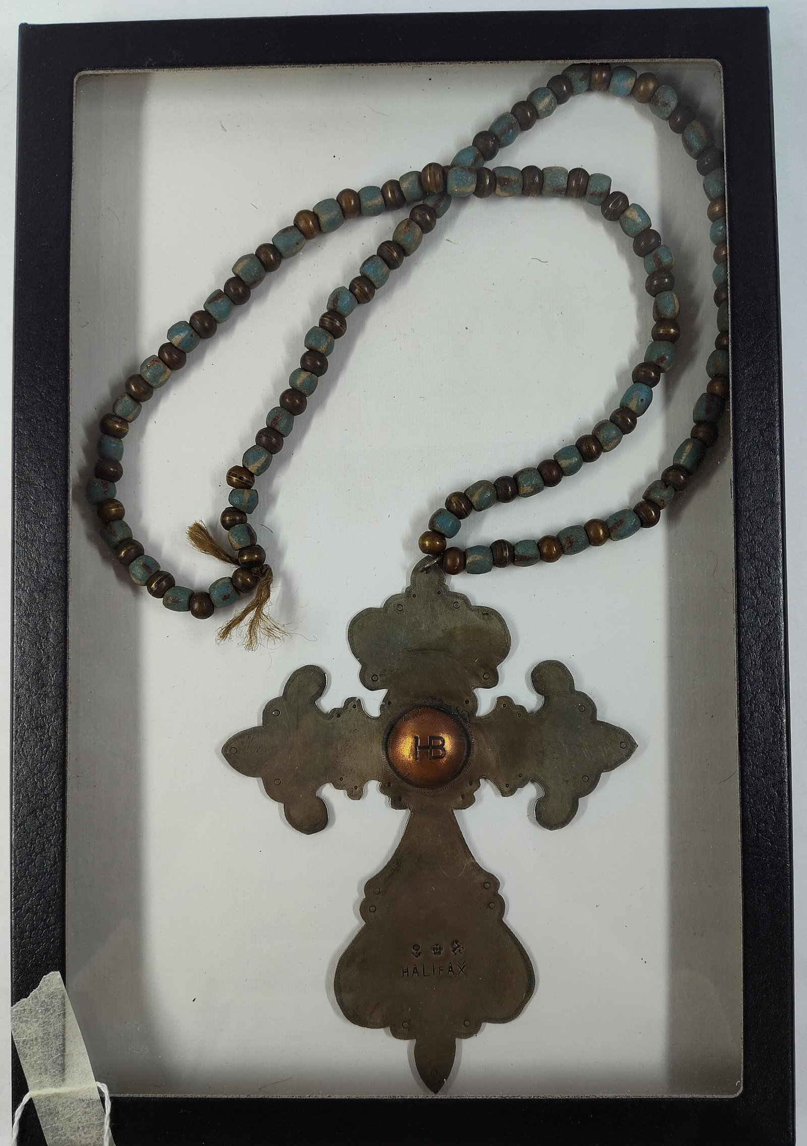 HB & Halifax Trade-Style Metal Cross Necklace: This decorative metal cross pendant is presented on a beaded necklace within a black shadow box frame. The cross is constructed from a grey-toned base metal and features a central, raised