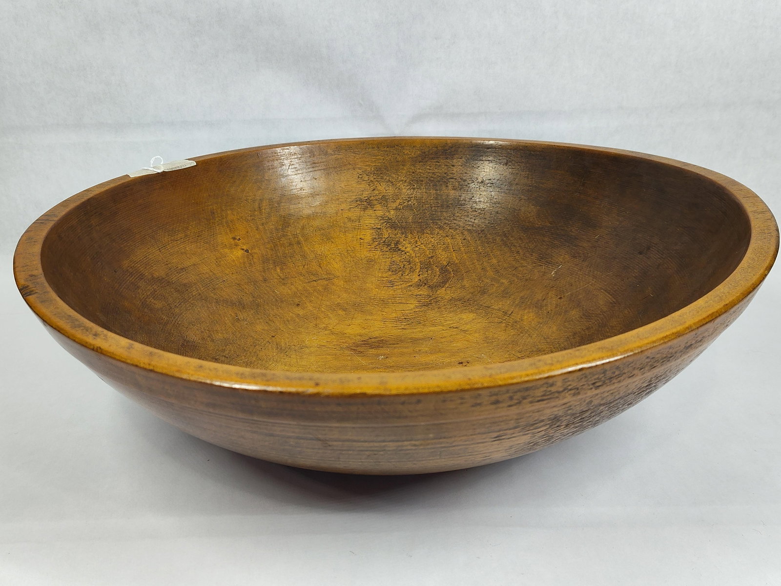 Large Antique Hand-Turned Hardwood Bowl: This large, lathe-turned bowl is crafted from a single piece of unidentified hardwood. It features a wide, shallow, circular form with a slightly thickened rim. Both the interior and exterior