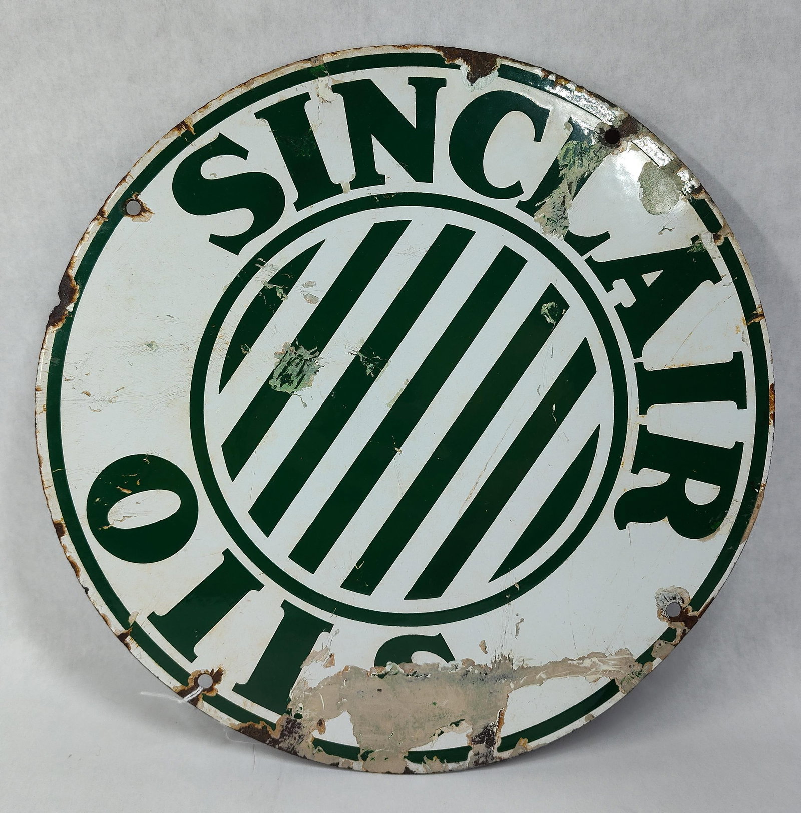 Sinclair Oils Porc. Enamel Advertising Sign: 12 inch diameter. A circular single-sided porcelain enamel advertising sign for Sinclair Oils, often used as a gasoline pump plate. The sign features a white field with dark green graphics and text.