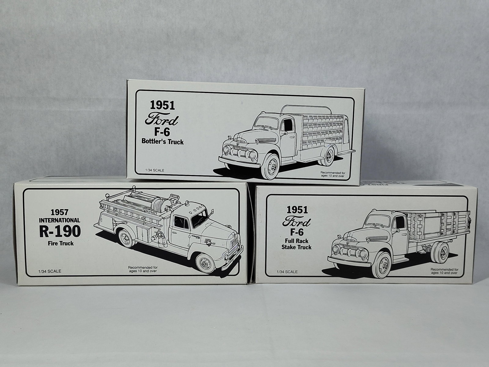 Three First Gear 1/34 Scale Die-Cast Model Trucks: A trio of First Gear 1/34 scale die-cast metal model trucks, each accompanied by its original white retail box and polystyrene foam interior packaging. The group includes two 1951 Ford F-6 models and