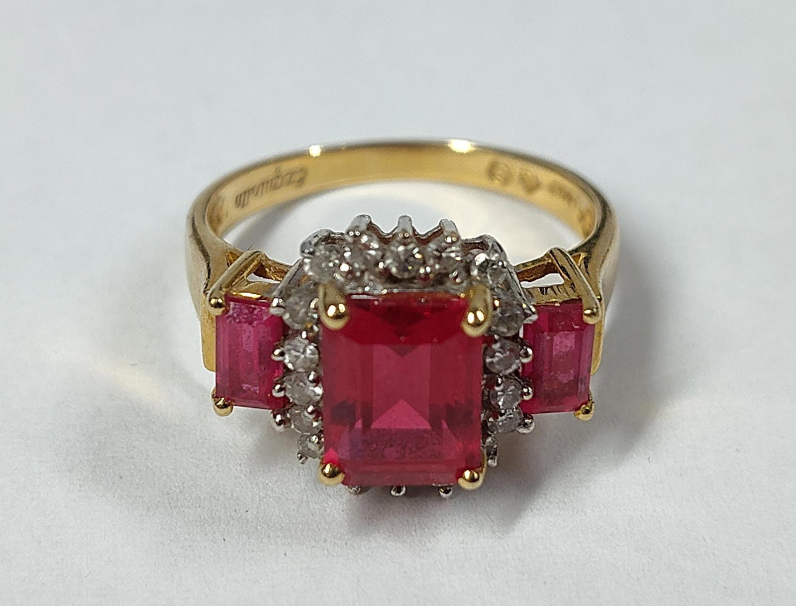 14K Yellow Gold Red & Colorless Stone Ring: A 14 karat yellow gold cocktail ring by Exquisite. The piece features a three-stone design consisting of three rectangular emerald-cut red stones. The central stone is highlighted by a cluster of