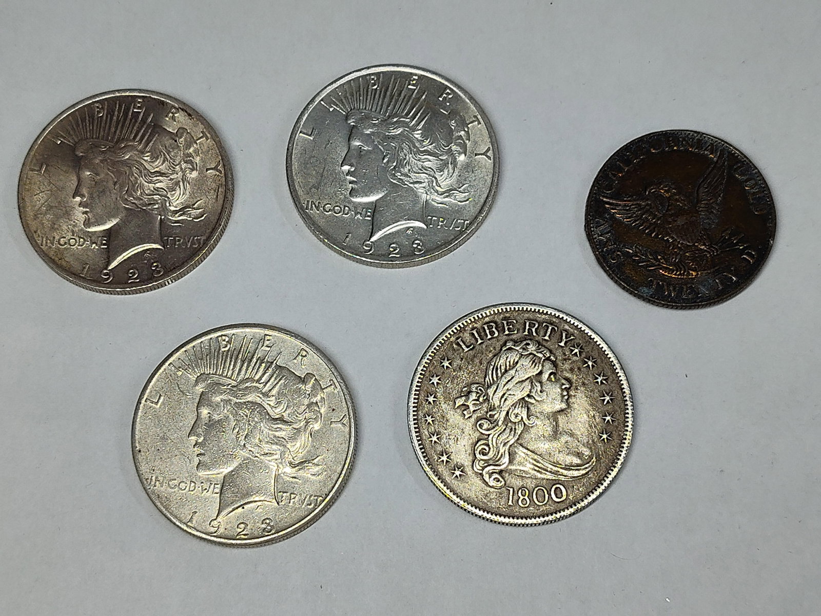 US Silver Peace Dollars & Numismatic Replicas: A collection of US Peace Dollars and related numismatic reproductions. The 1923 dated Peace Dollars are struck in 90 percent silver with reeded edges, featuring the standard Liberty head obverse and