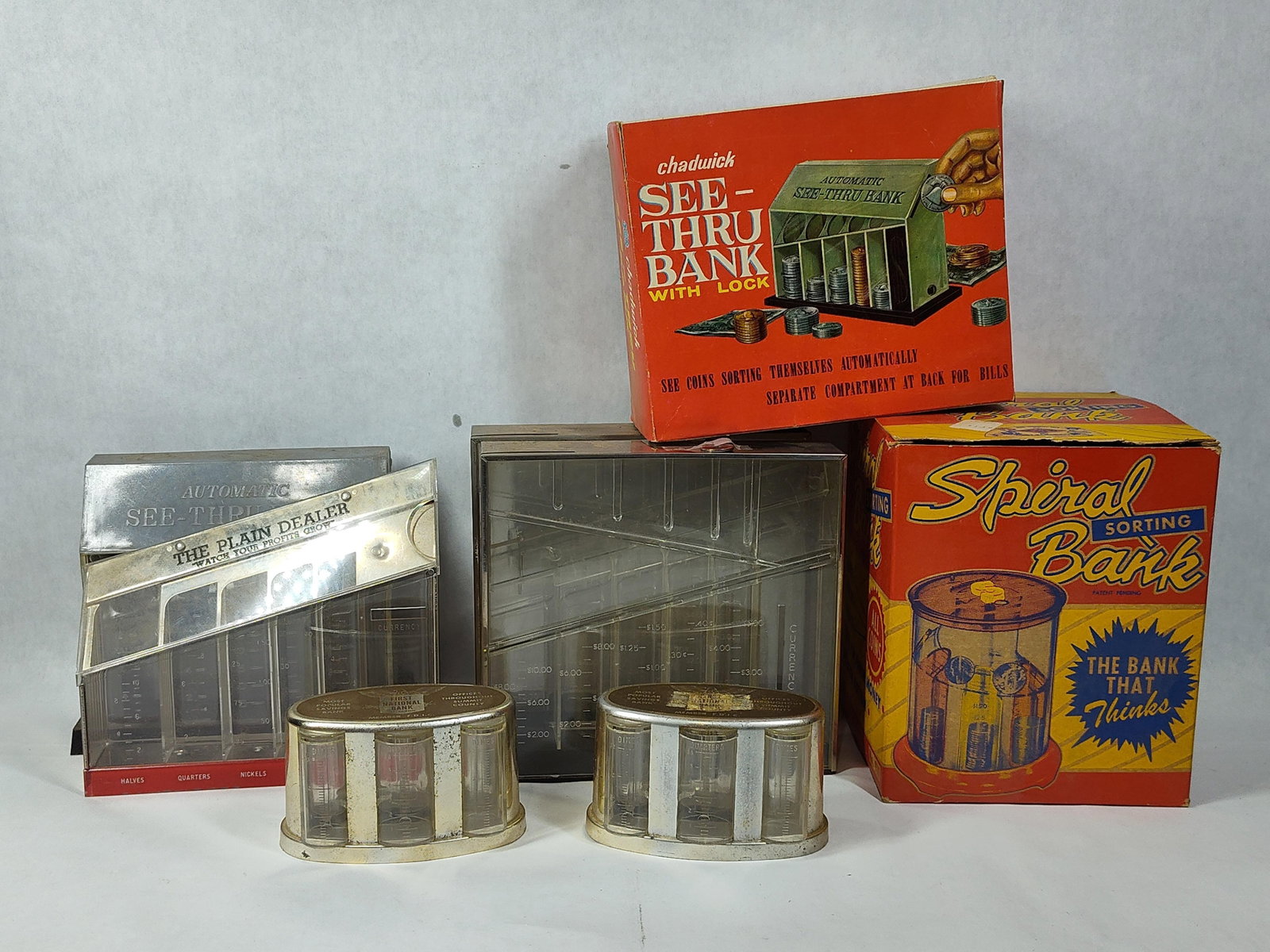 Set 7 Mechanical & Still Coin-Sorting Banks: This lot features a collection of seven coin-sorting banks produced in the mid-20th century. The collection includes two examples in their original retail packaging: a Chadwick See-Thru Bank and a