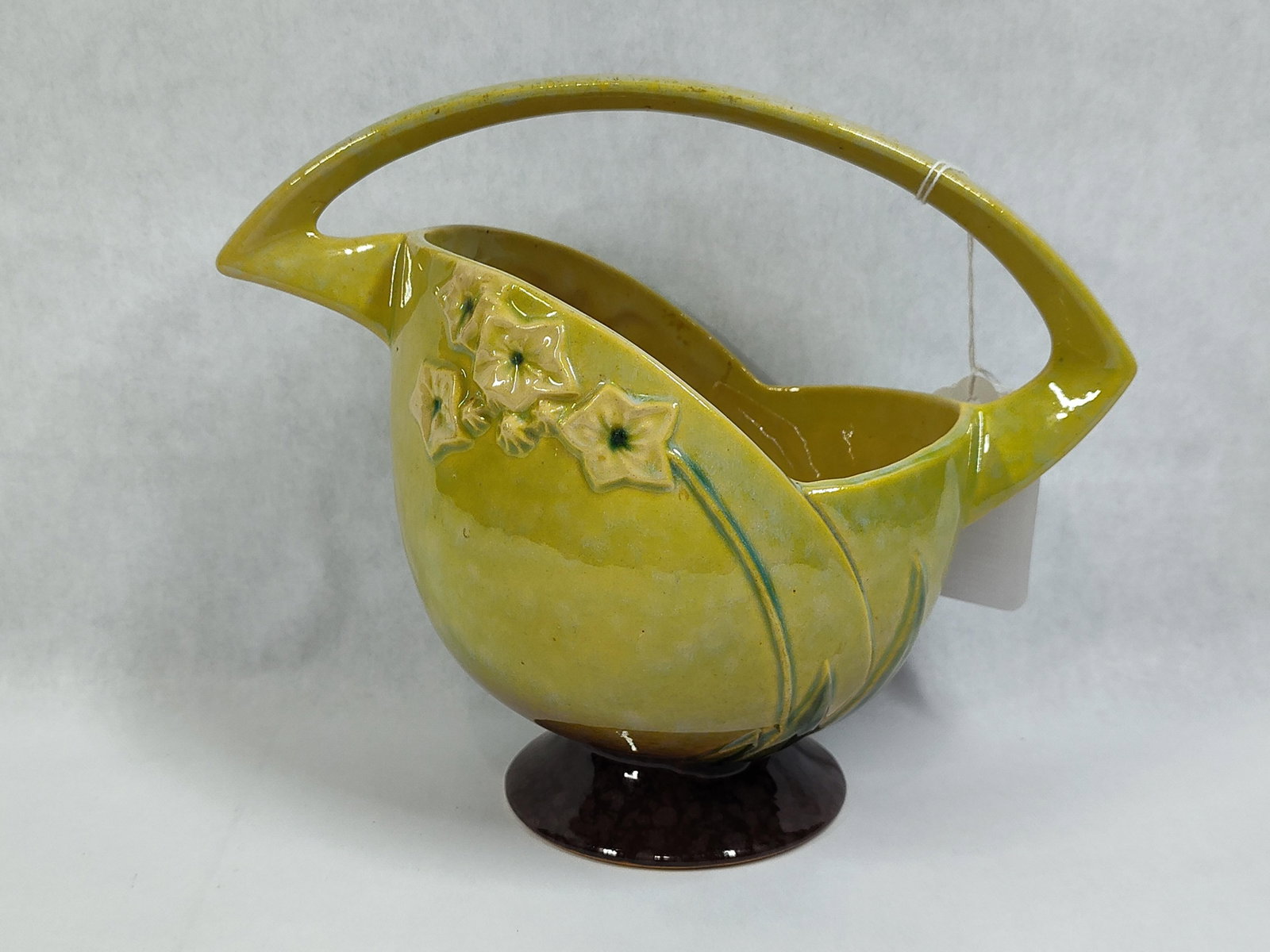 Roseville Pottery Wincraft Chartreuse Basket 208-8: This piece of American art pottery is a footed basket manufactured by Roseville Pottery in the Wincraft pattern, which was introduced in 1948. The vessel is constructed of earthenware and features a