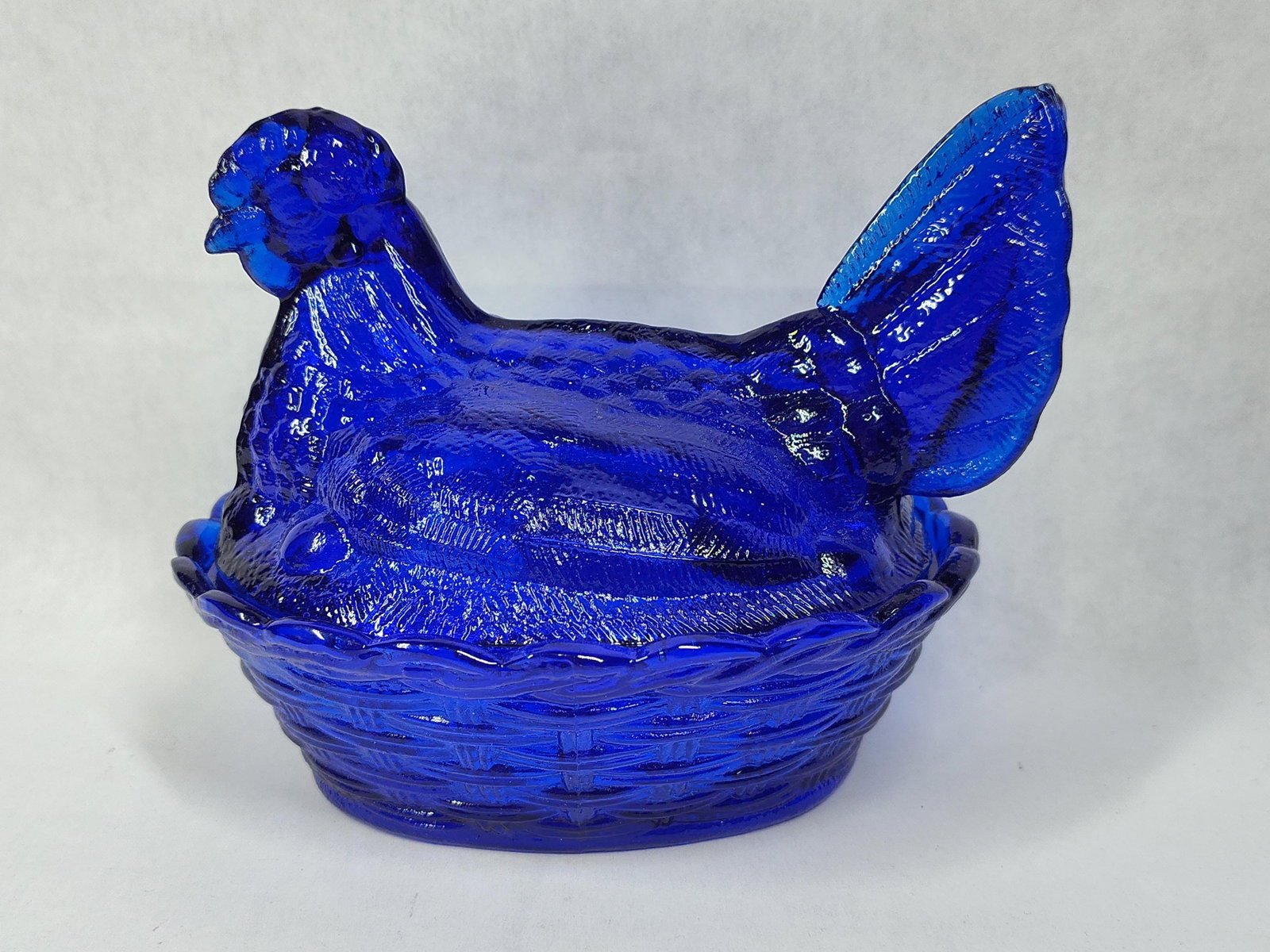 Cobalt Blue Glass Split-Tail Hen on Nest: A two-piece pressed glass covered dish executed in deep cobalt blue glass. The lid is fashioned in the form of a nesting hen, featuring a distinctive split tail, detailed feathering throughout the