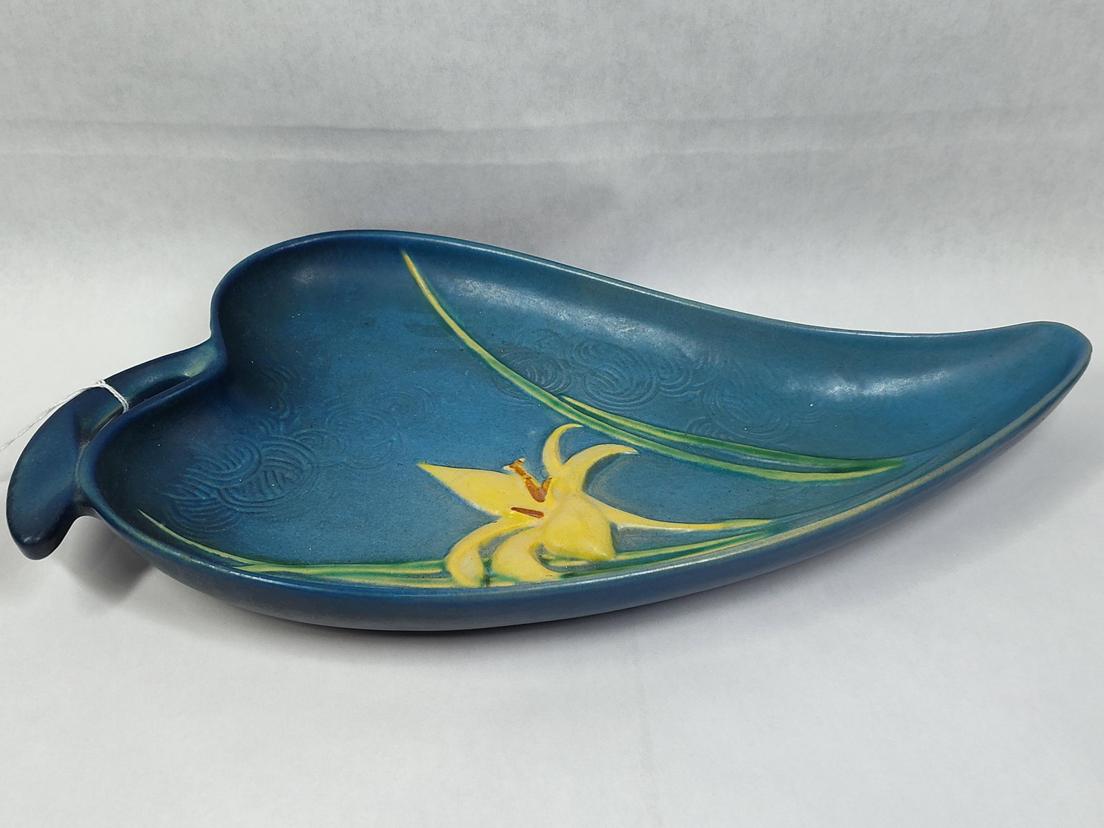 Roseville Pottery Zephyr Lily Blue Leaf Tray 477: This American art pottery leaf-shaped tray was produced by Roseville Pottery as part of the Zephyr Lily line, which was introduced in 1946. Crafted from earthenware, the elongated vessel features a