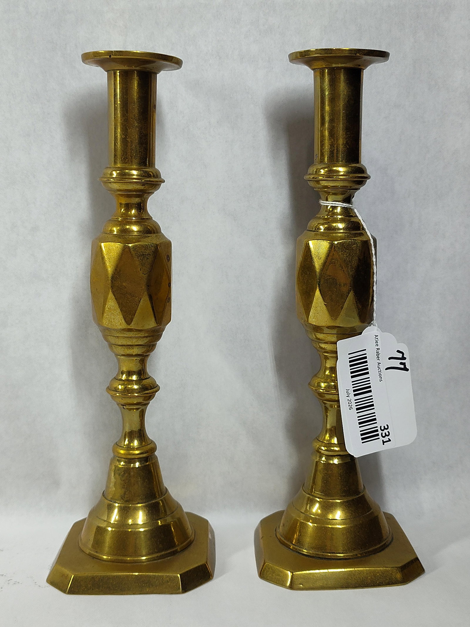 Pair Diamond Princess Victorian Brass Candlesticks: A pair of cast brass candlesticks in the Diamond Princess pattern. Each piece features a traditional baluster form, beginning with a circular sconce and flared rim set upon a ring-turned stem. The