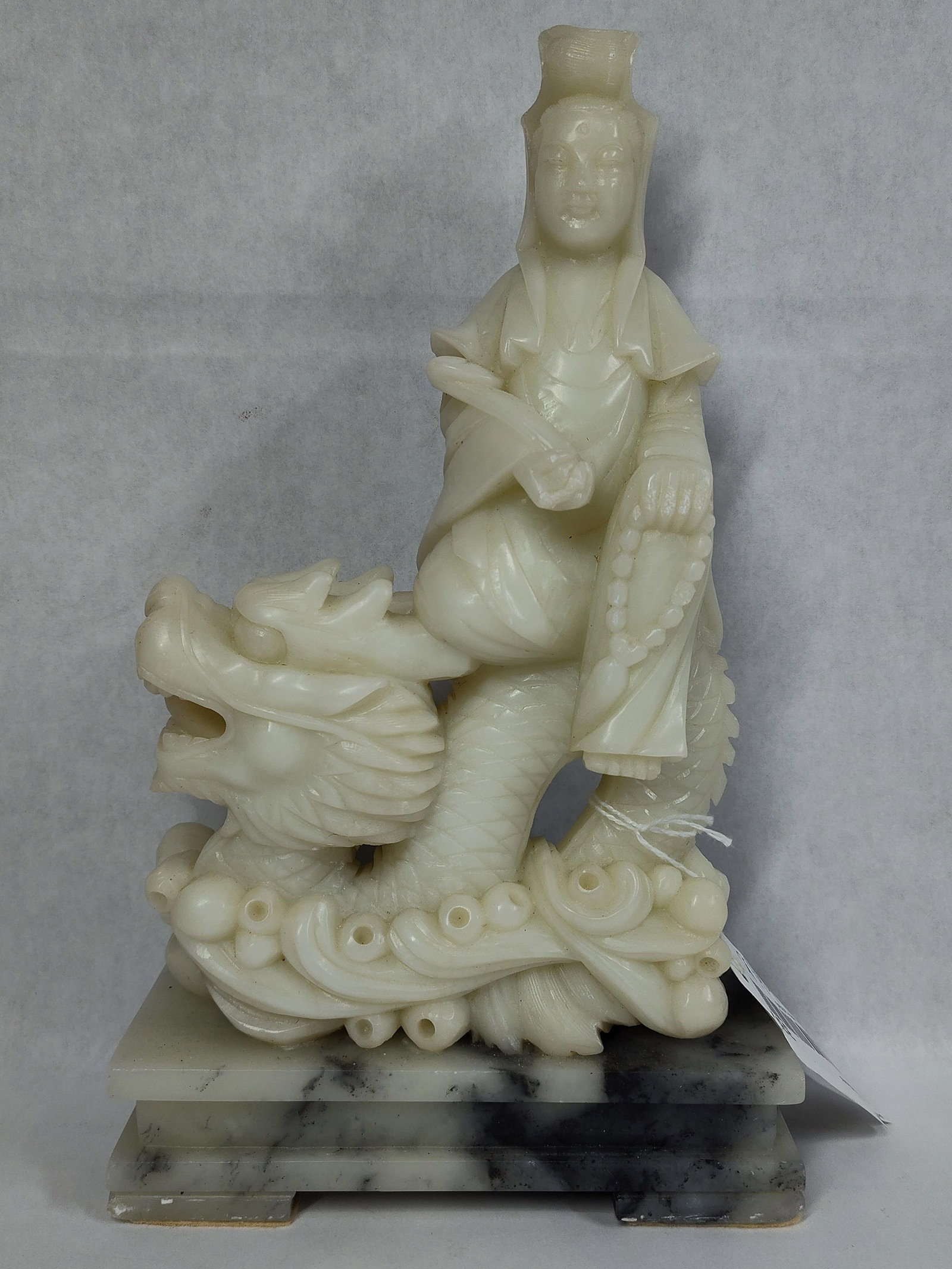 Chinese Hardstone Figure of Guanyin on Dragon: This carved hardstone figure depicts Guanyin, the Bodhisattva of Compassion, in a traditional pose riding a dragon. The figure is rendered in a cream-colored to off-white hardstone, possibly bowenite