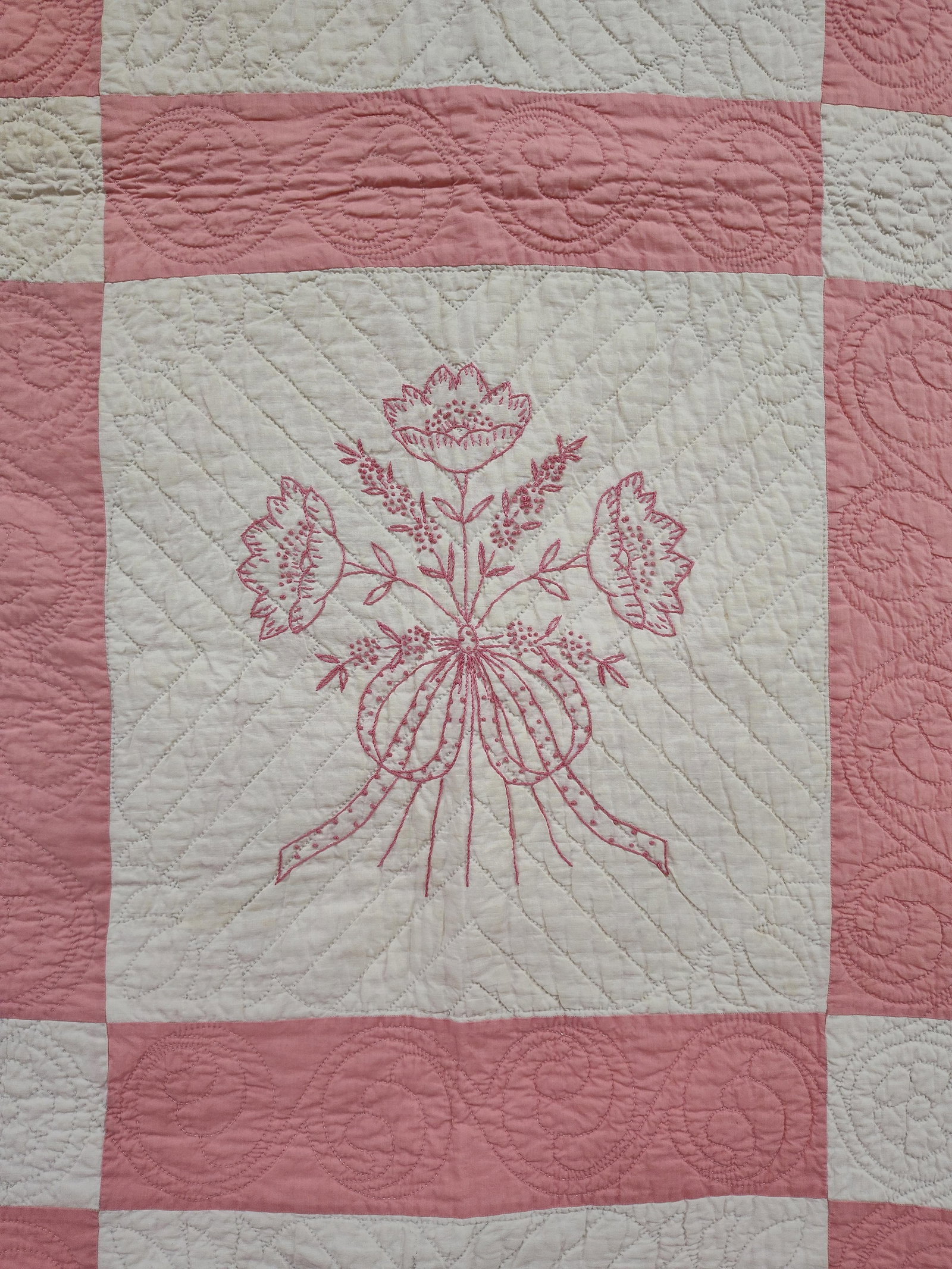 American Hand-Embroidered Floral Bouquet Quilt: This is a mid-20th-century American cotton quilt featuring twelve white fabric blocks set into a pink sashing grid with white cornerstones and a wide pink border. Each central block is decorated with