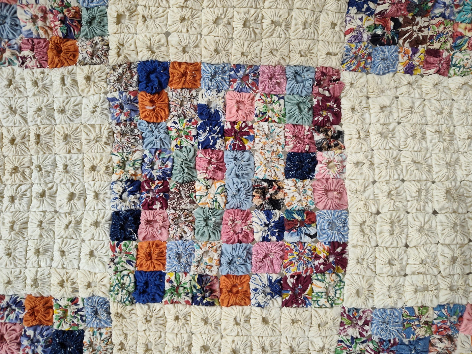 Hand-Stitched Yo-Yo Checkerboard Feedsack Quilt: This hand-stitched yo-yo quilt features a checkerboard pattern alternating between solid cream-colored blocks and multi-colored scrap blocks. Each larger square block is constructed from a seven-by-se