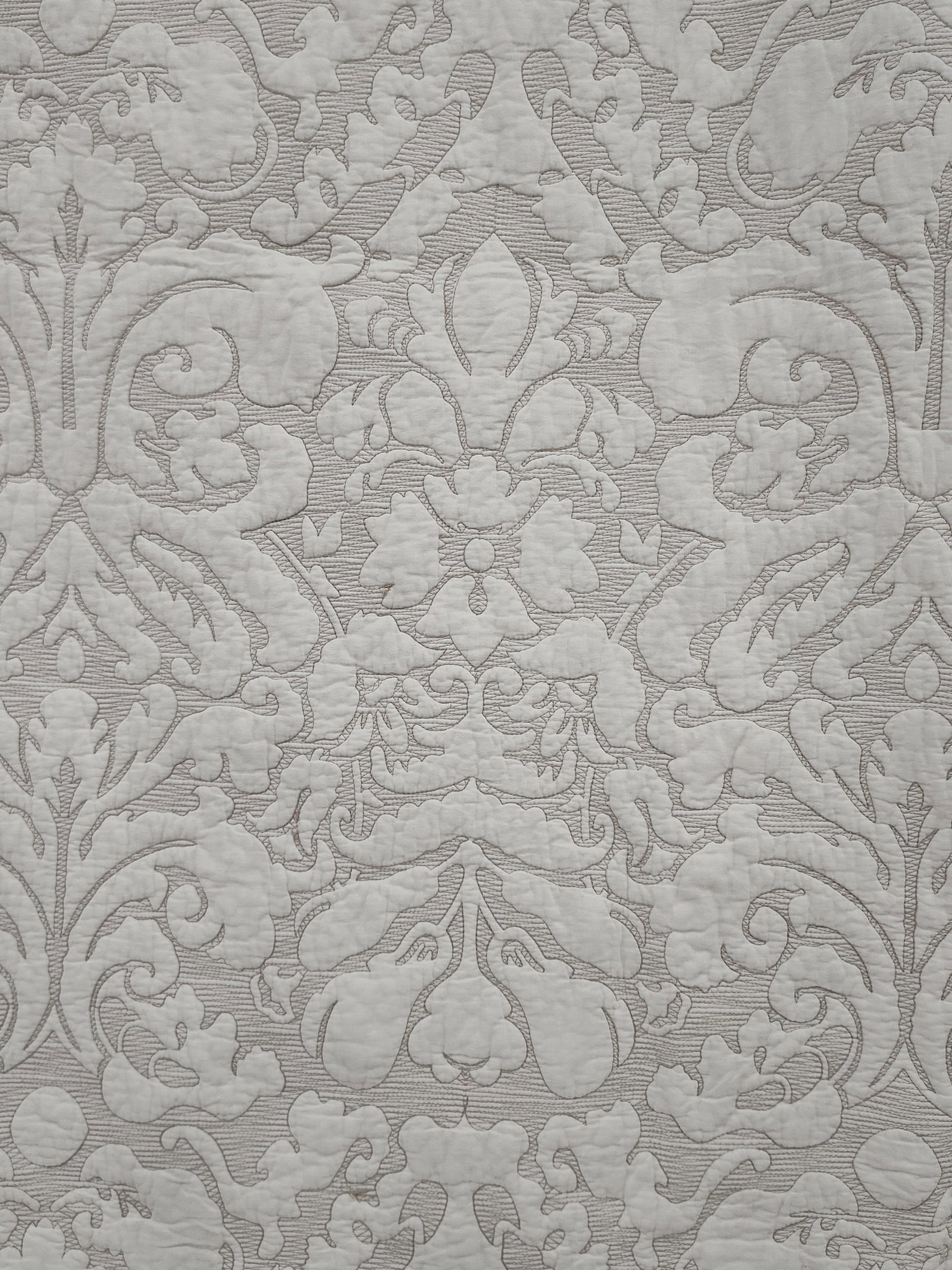 White Matelasse Damask Machine Quilted Coverlet: This textile is a large-scale wholecloth quilted coverlet or bedspread in an off-white color. The design features a repeating damask pattern characterized by scrolling acanthus leaves, floral blossoms