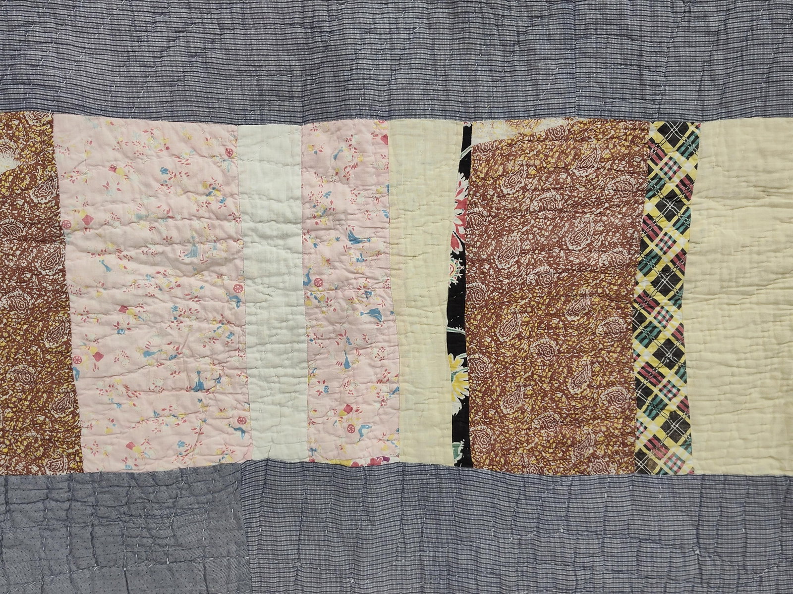 Mid-20th C. American Strip-Pattern Scrap Quilt: A mid-20th century American hand-quilted utility or scrap quilt. The piece is constructed in a horizontal strip-style pattern, featuring rows of varied vertical fabric patches alternating with