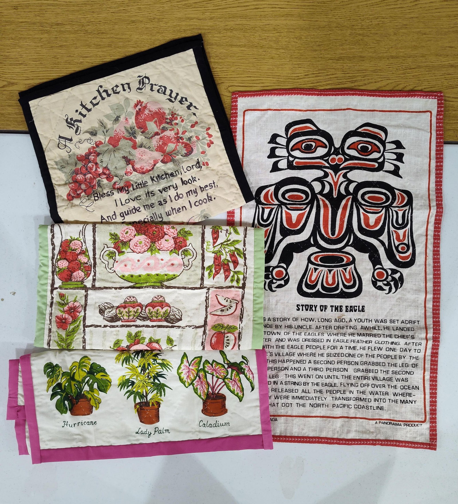 Panorama Product NW Coast Tea Towel & Quilted Mats: This lot comprises four vintage printed textiles. The first item is a printed linen tea towel featuring a bold Northwest Coast Indigenous style eagle design in black and red. Below the graphic is a