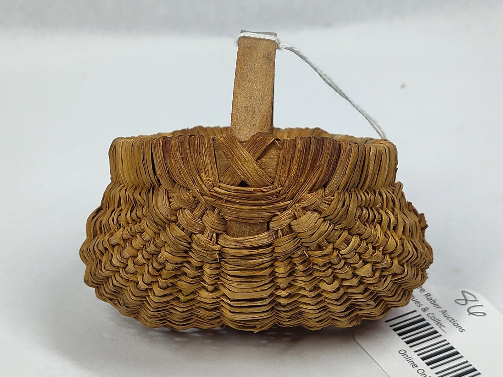 Splint Porcupine Weave Buttocks Basket: A miniature 4in hand-woven basket featuring a traditional buttocks or ribbed construction. The piece is crafted from natural wood splints, with a solid bentwood handle and rim. The exterior is decorat