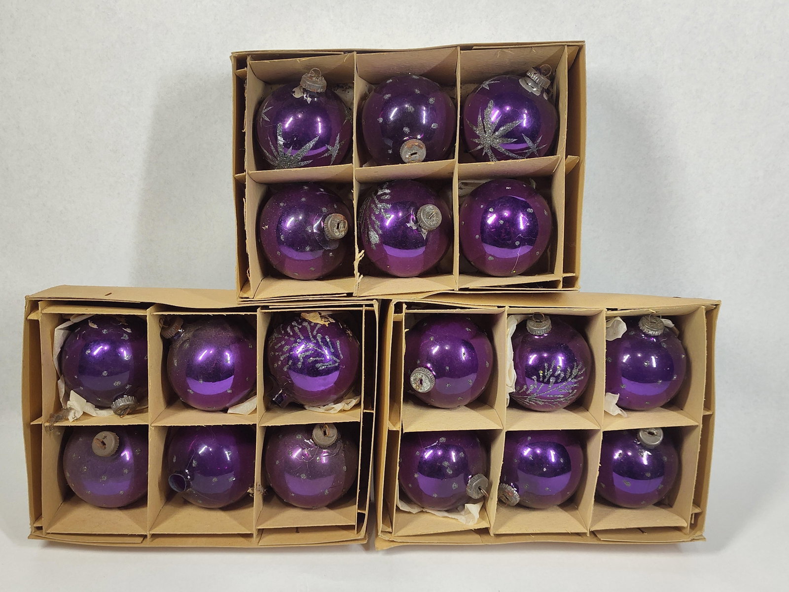 18 Purple Glass Christmas Ornaments: A collection of eighteen (18) vintage spherical glass Christmas ornaments, presented in three original cardboard storage boxes. The ornaments feature a deep purple or amethyst finish, with several exa