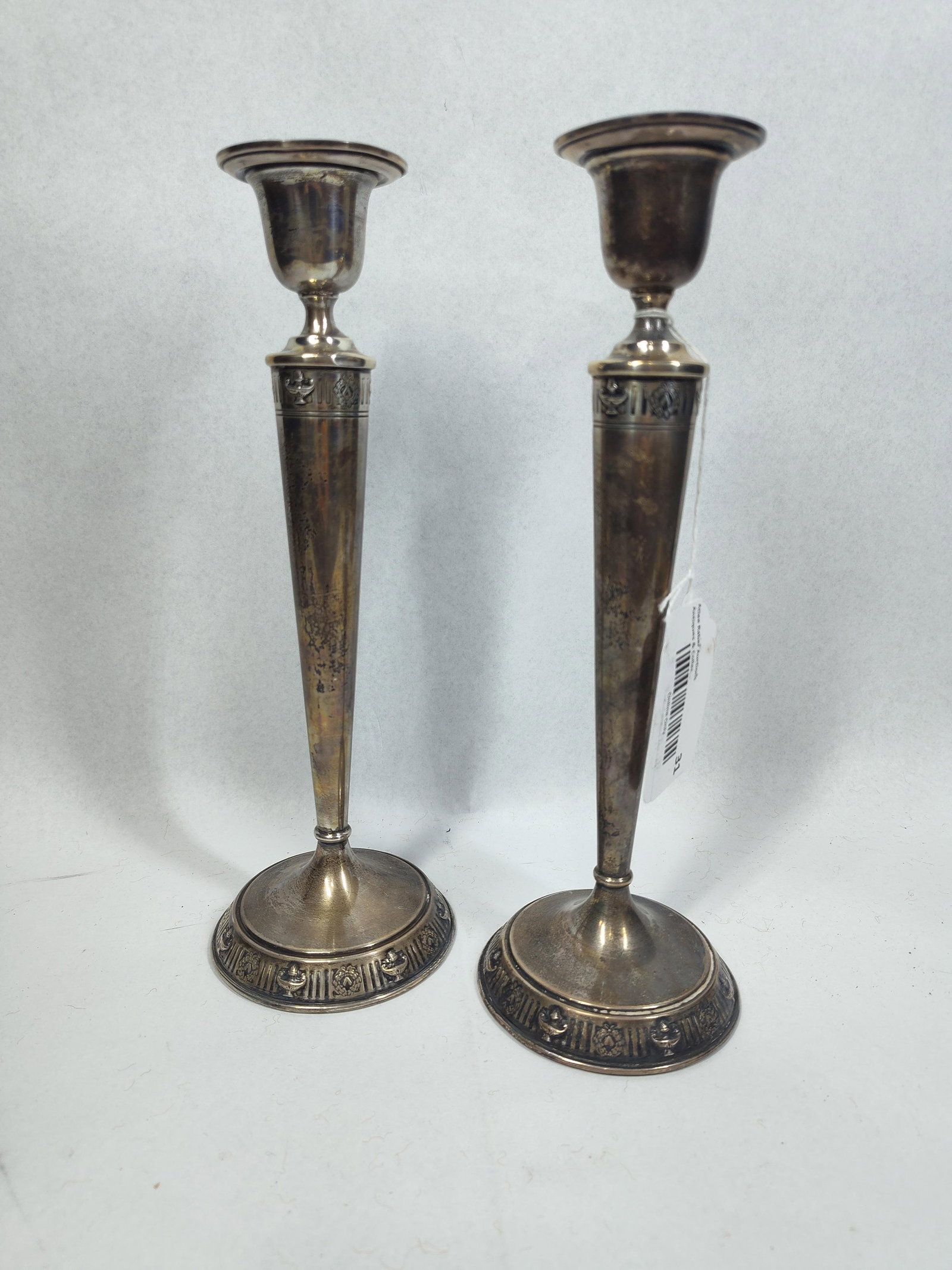 Neoclassical Sterling Candlesticks: 11in tall A pair of sterling silver candlesticks in the Neoclassical Revival style. Each piece features a slender, tapered circular stem rising from a stepped circular base. The candlesticks are