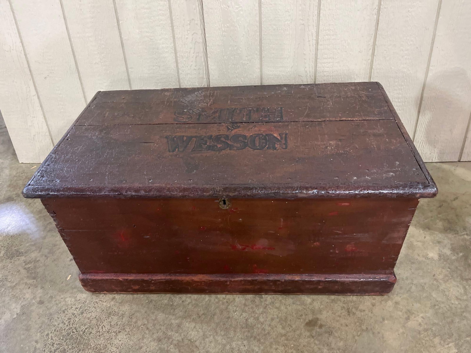 Smith & Wesson Stenciled Wood Chest: 37x21x17 This antique wooden storage chest is constructed of solid wood boards with a dark reddish-brown stained finish and molded edges on the lid and base. The top of the lid features black stencile