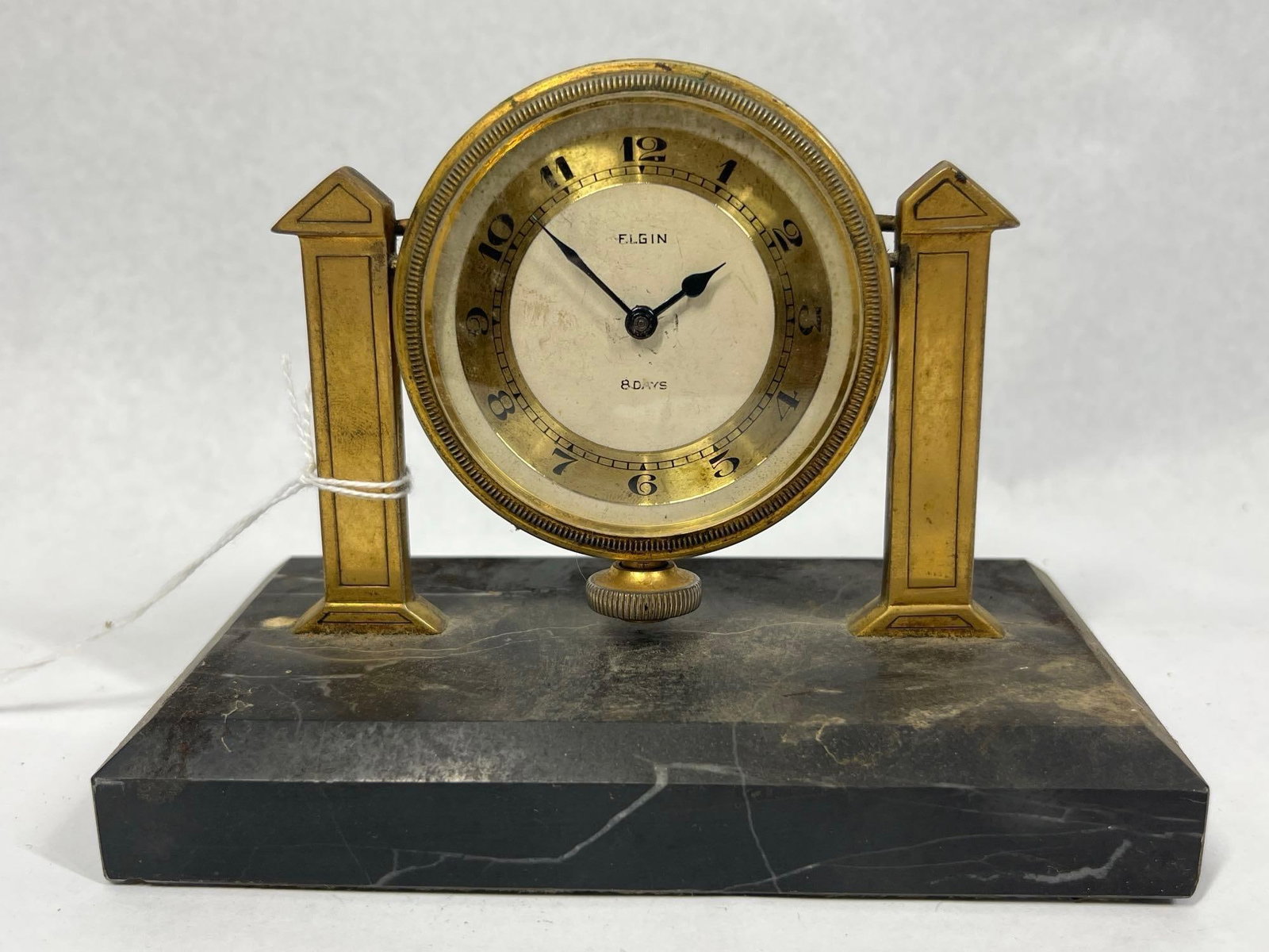 Elgin Art Deco Brass/Marble Clock, 1931: This Art Deco desk clock features an eight-day mechanical movement manufactured by the Elgin National Watch Company. The circular brass-toned metal case is suspended between two geometric pylon-style 