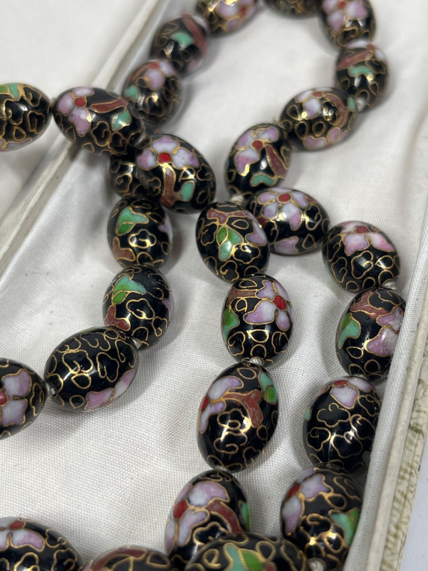 Chinese Export Cloisonne Bead Necklace: 32in long This vintage Chinese export-style necklace features cloisonne enamel beads individually knotted on a white cord. The uniform oval beads are decorated with a traditional floral pattern, showi