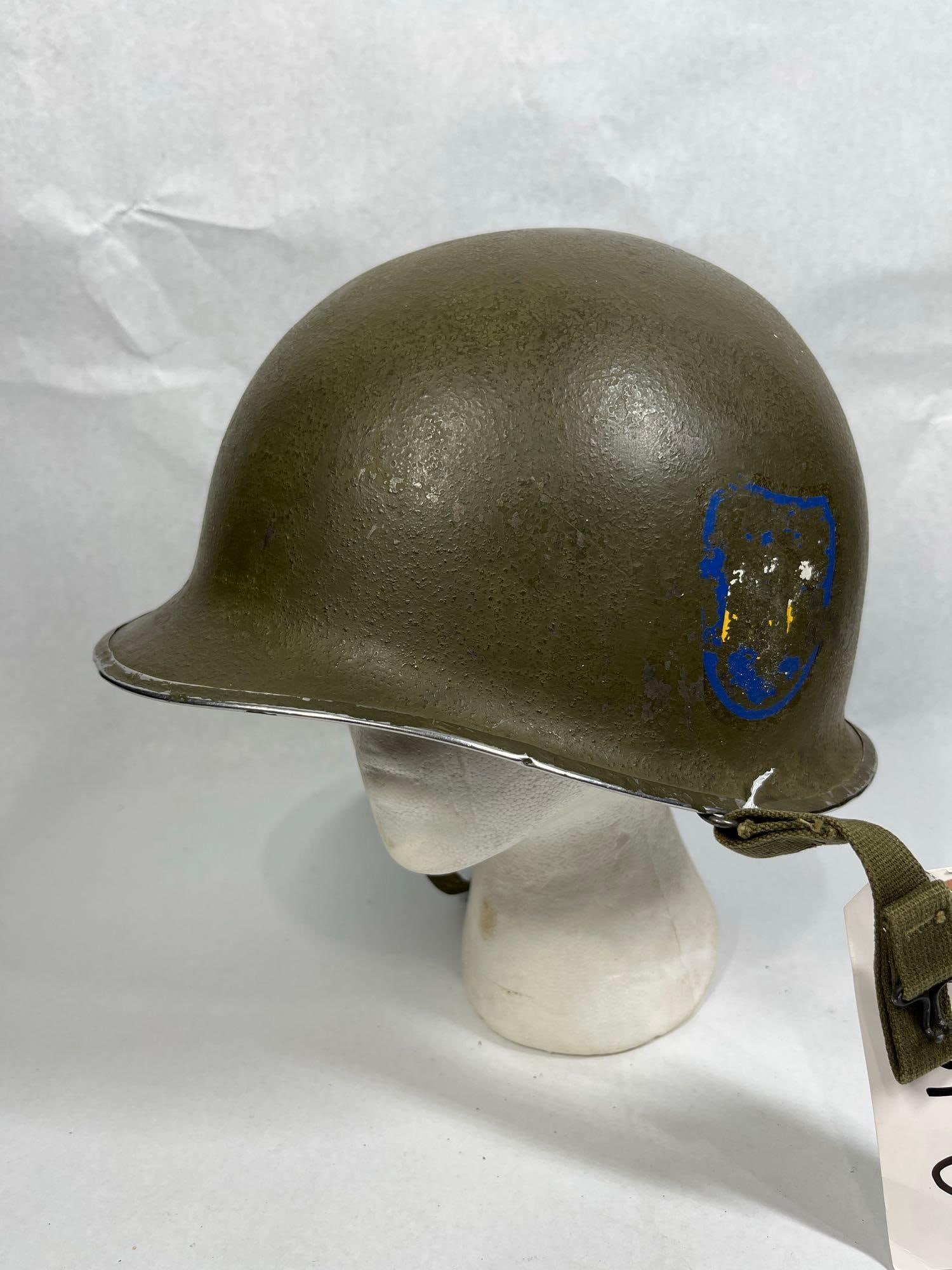 US Military Korean War M1 Steel Combat Helmet with Liner and Unit Insignia: This lot features a US military M1 steel combat helmet paired with a removable non-metallic liner. The steel shell is a front-seam variety with a stainless steel rim, consistent with manufacture