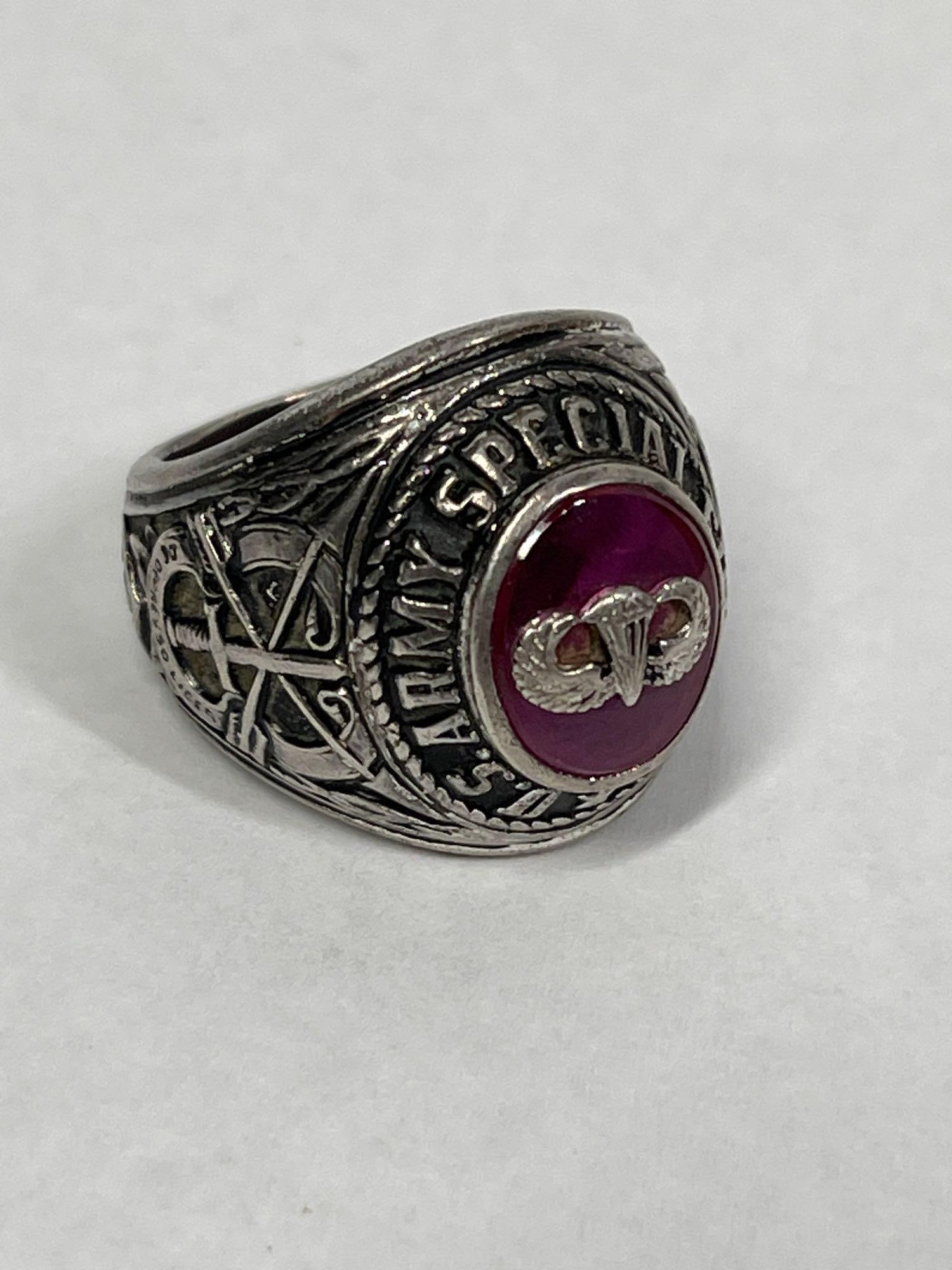 U.S. Army Special Forces Airborne Commemorative Signet Ring in Silver-Toned Metal: A U.S. Army Special Forces commemorative signet ring, crafted from a silver-toned metal. The centerpiece features a faceted red stone, likely a synthetic ruby, with an applied silver-toned Parachutist