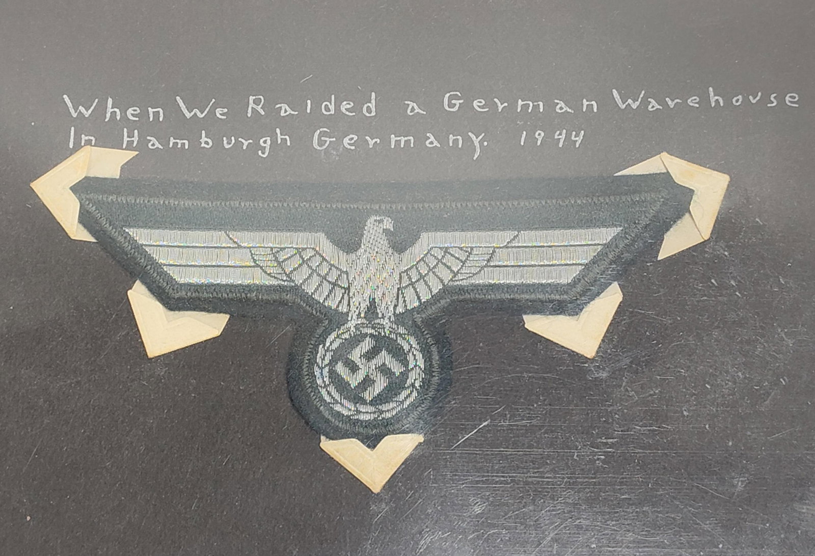 WWII German Waffen-SS Machine-Embroidered Breast Eagle with 1944 Hamburg Provenance: This lot features a World War II German Waffen-SS machine-embroidered breast eagle, known as a Hoheitsabzeichen. The insignia is constructed with silver-gray rayon thread machine-embroidered onto a da
