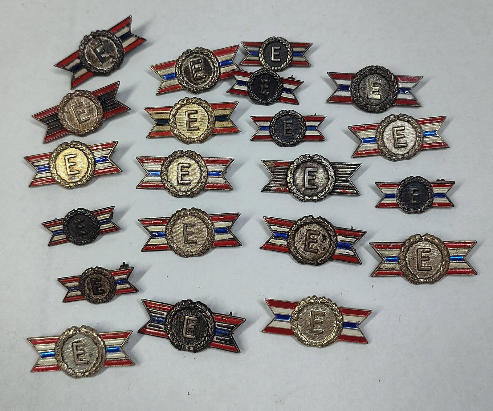 A Collection of WWII Sterling Silver Enameled Army-Navy Production E Award Lapel Pins: A collection of enameled and sterling lapel pins awarded to civilian war workers during World War II for industrial excellence. Each pin is designed as a horizontal banner with red, white, and blue en