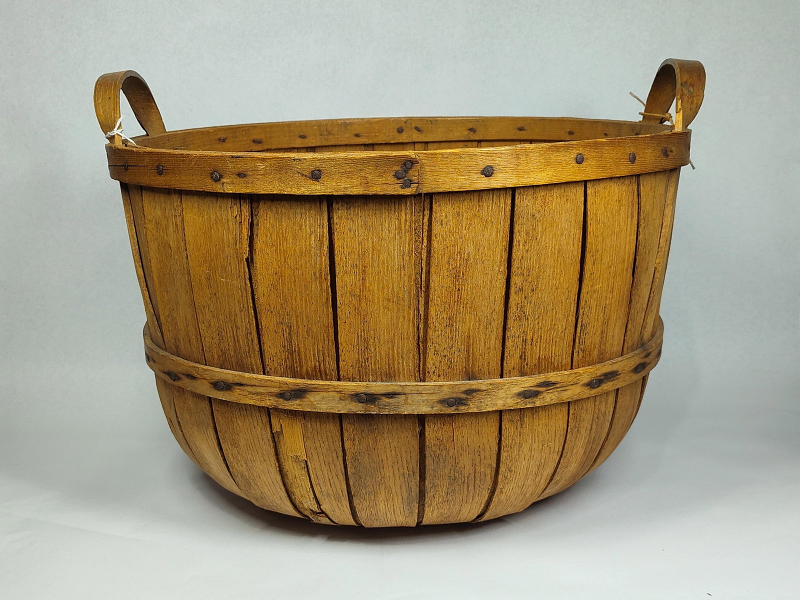 Antique Oak Stave Gathering Basket: 18in dia. This is an antique or vintage gathering basket, constructed using the stave method. The body consists of vertical wooden slats, likely oak, which are secured with metal tacks to a flat,
