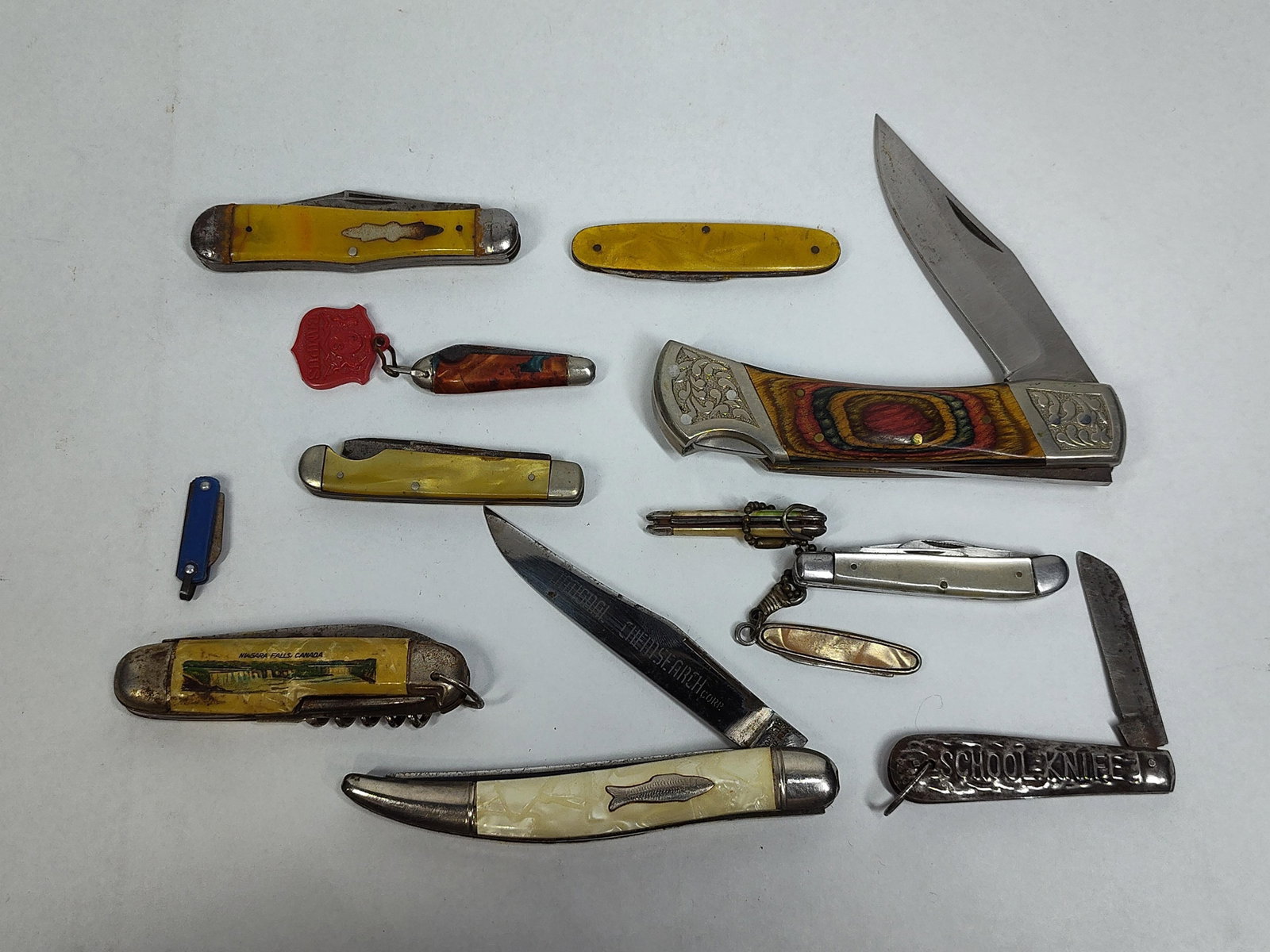 12 Imperial & Souvenir Pocket Knives: A collection of twelve assorted vintage and modern folding pocket knives featuring various styles and handle materials. The lot is highlighted by an Imperial single-blade folder with curved pearlescen