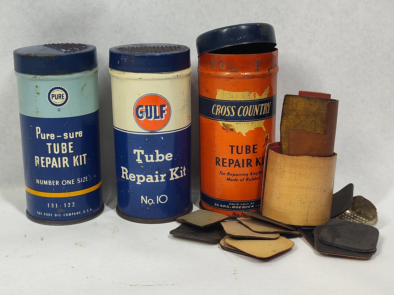 Gulf, Pure Oil & Sears Tube Repair Tins: This lot comprises three vintage lithographed tin automotive tube repair kits dating from the mid-20th century. These kits represent essential roadside accessories used during the era of tube-type tir