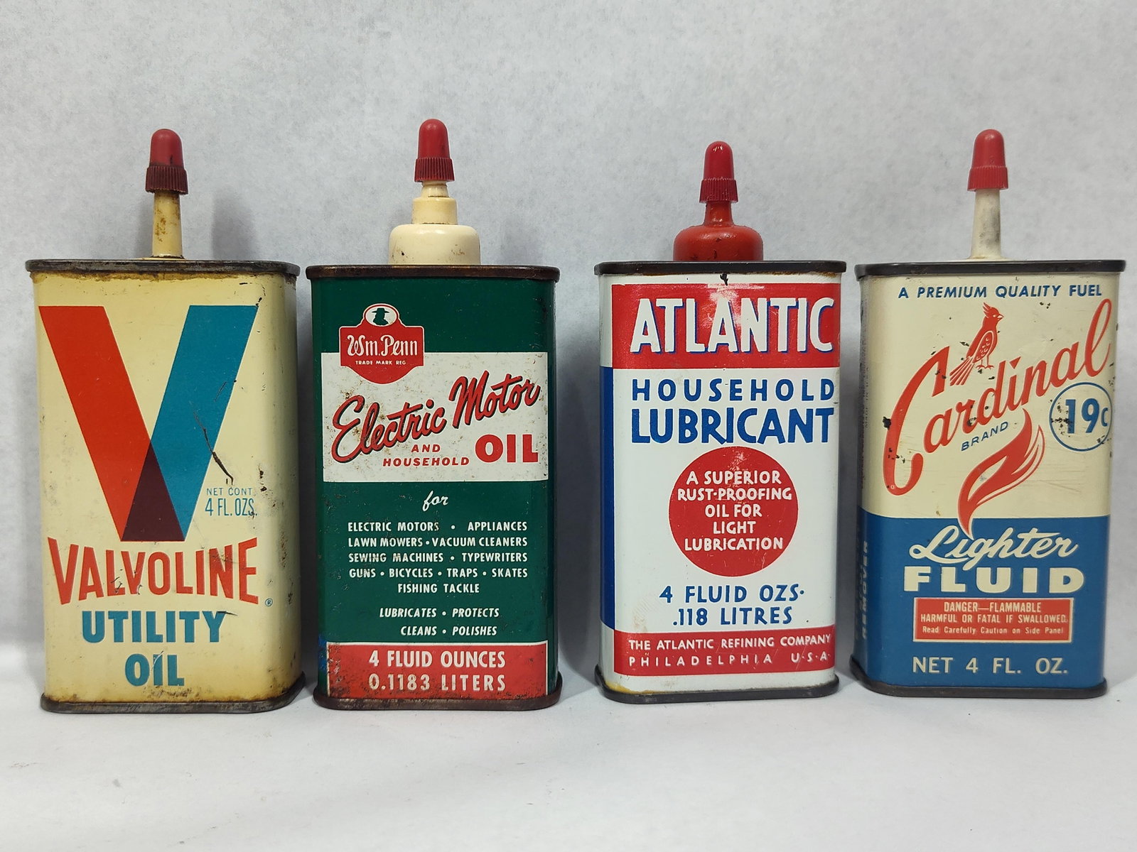 Set 4 Oil & Lighter Fluid Cans: A collection of four vintage lithographed lubricant and fuel containers, each featuring a rectangular body, plastic spout, and red screw-on cap. The assortment includes a Valvoline Utility Oil tin fro