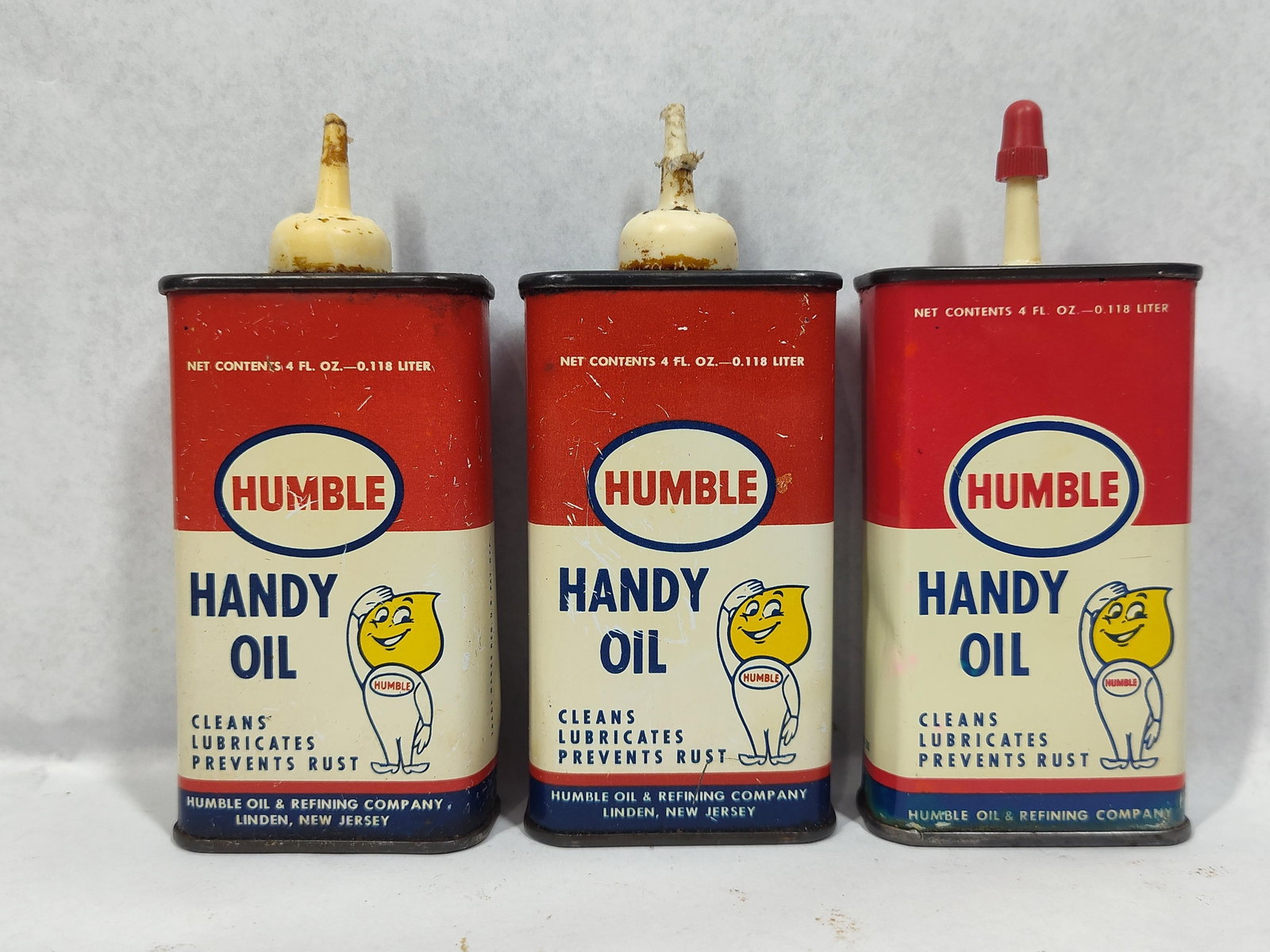 Trio Humble Handy Oil Cans: This lot features a trio of vintage 4-fluid-ounce lubricant cans produced by the Humble Oil & Refining Company of Linden, New Jersey. Each lithographed tin container features a red, white, and blue co
