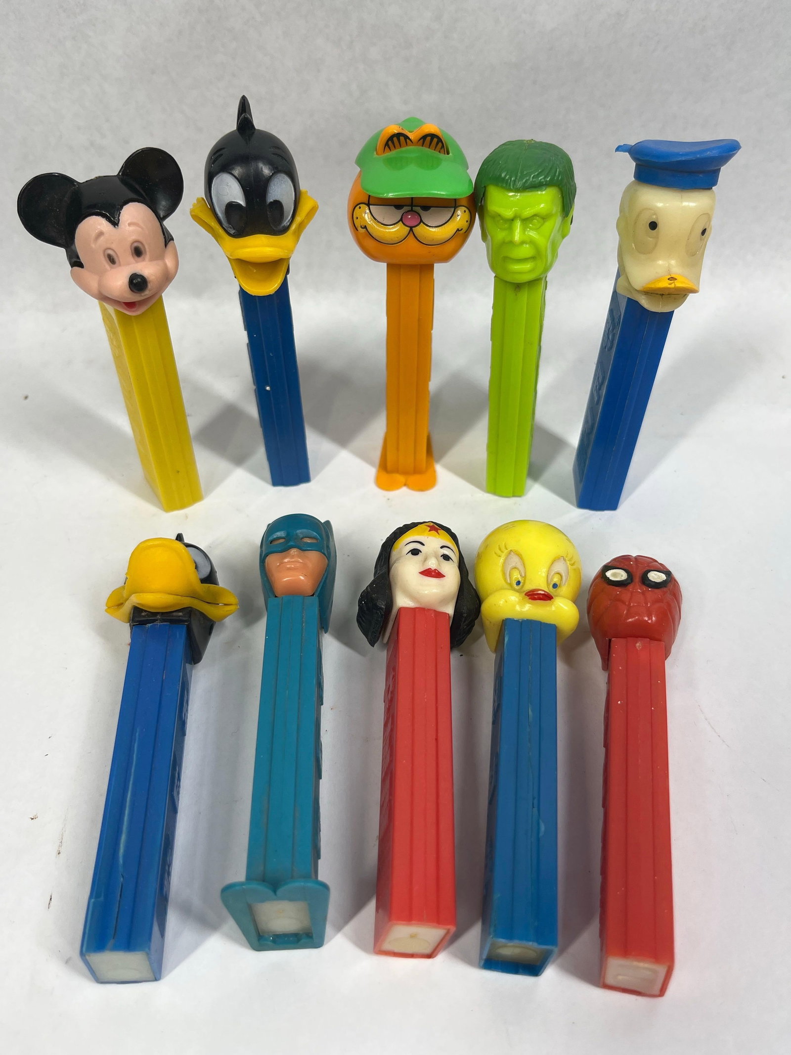 10 PEZ Disney/Tunes/Hero Dispensers: A collection of ten authentic vintage PEZ dispensers manufactured by PEZ. These items are constructed from molded plastic and feature various licensed characters. The group includes Mickey Mouse on a