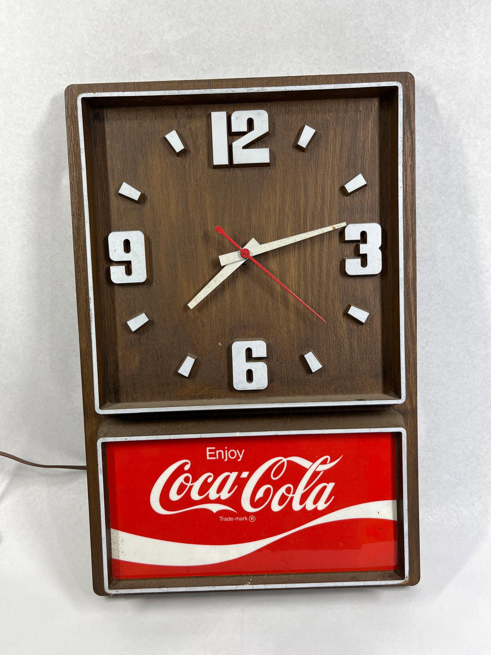 Impact Int Coca-Cola Electric Clock: 18x12 This rectangular advertising wall clock was manufactured by Impact International Inc. of Carson City, Nevada. The housing is constructed from molded plastic with a dark faux-woodgrain finish.