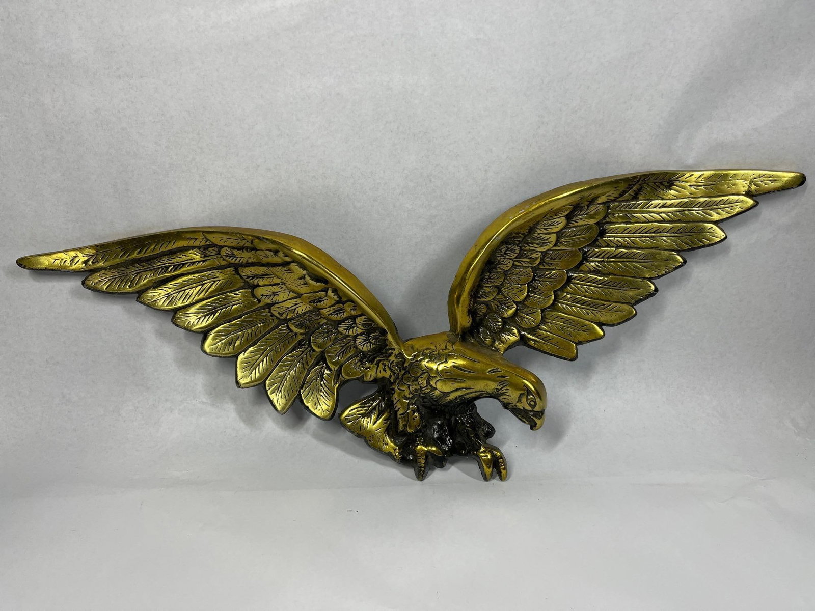 Lou Shell Metal American Eagle Plaque: 26in wide A mid-century decorative wall plaque by Lou Shell depicting an American bald eagle. The piece is cast from a metal alloy, featuring a gold-toned finish over a dark base. The eagle is